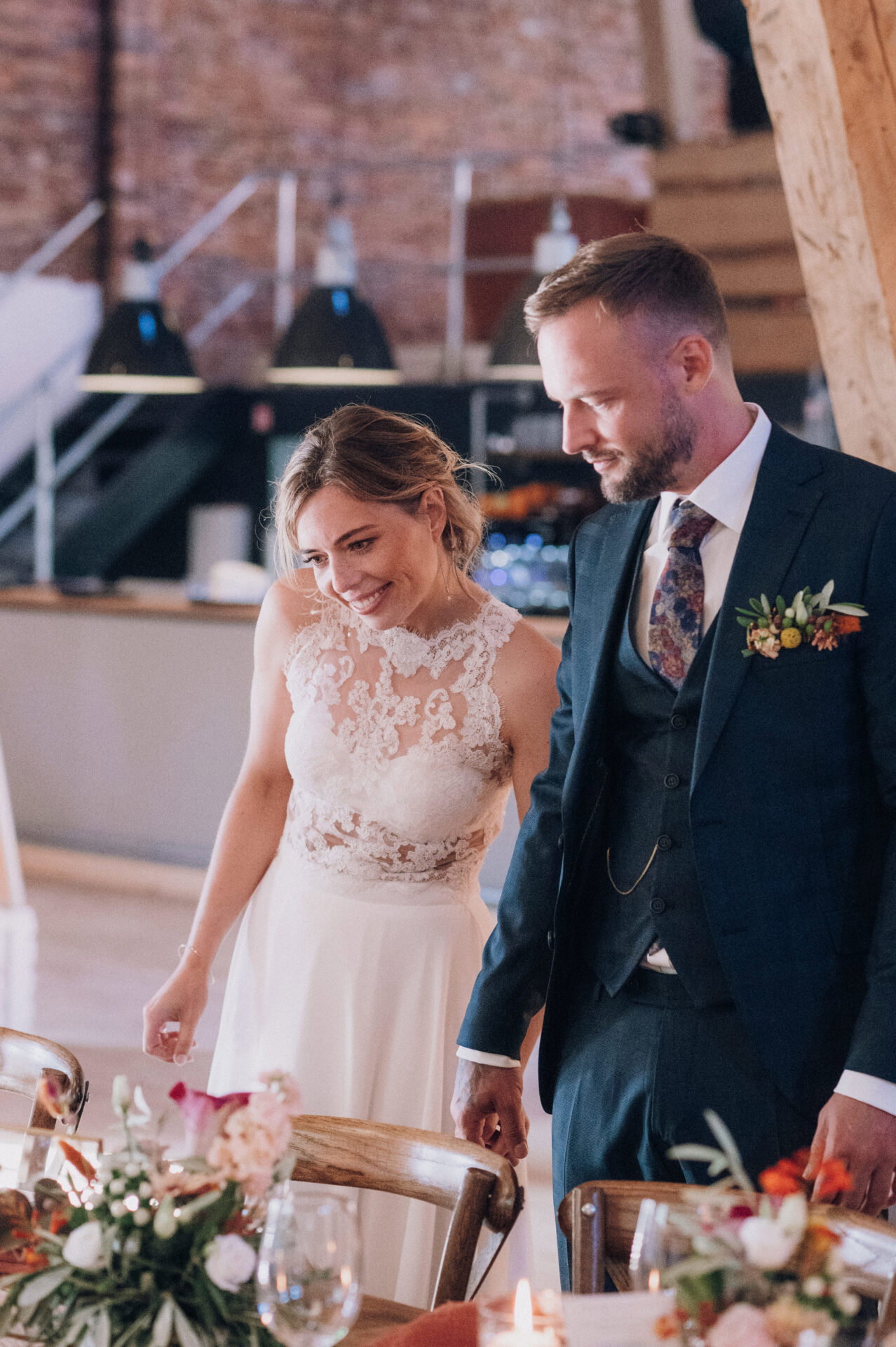 Ein intimer Moment: Die Braut und ihr Bräutigam stehen an der festlich gedeckten Tafel und lassen den Anblick ihrer Hochzeitsdekoration auf sich wirken. Die warmen Farben der Blumen und Kerzen schaffen eine gemütliche und festliche Stimmung.