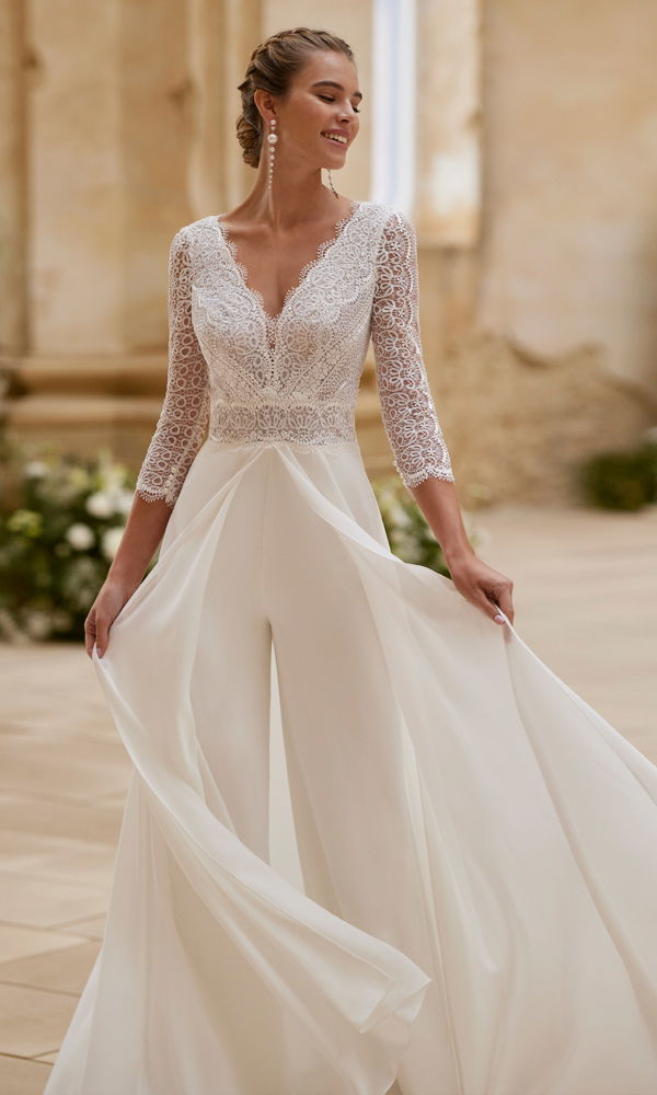 Moderne Braut im luftigen Boho-Jumpsuit mit filigraner Spitze und weit schwingenden Stoffbahnen, ideal für unkonventionelle Hochzeiten.