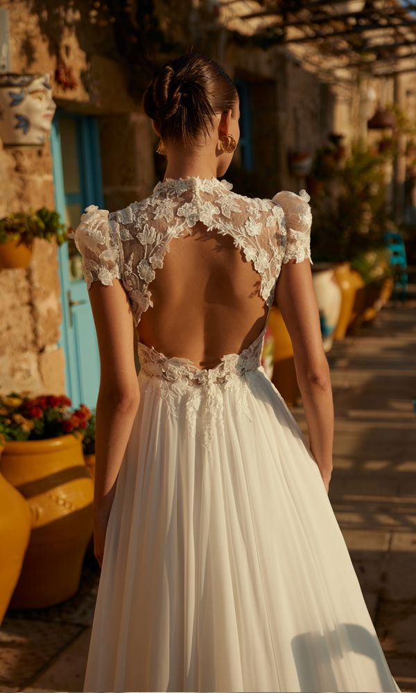 Romantisches Brautkleid mit zarter Spitze und offenem Rücken, aufgenommen in einem sonnigen Innenhof mit mediterranen Elementen.