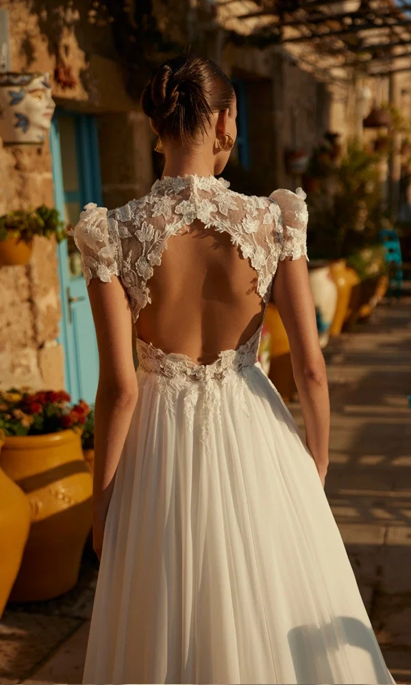 Romantisches Brautkleid mit zarter Spitze und offenem Rücken, aufgenommen in einem sonnigen Innenhof mit mediterranen Elementen.