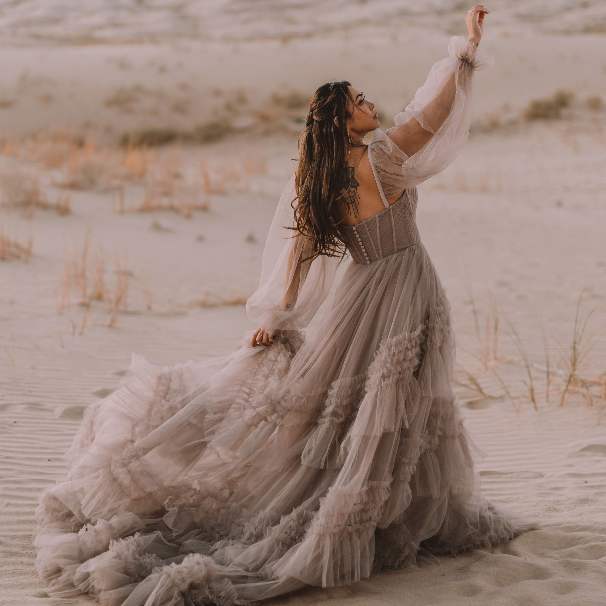 Elegantes, bodenlanges Hochzeitskleid mit luftigen Ärmeln und Lagen aus Tüll, eingefangen in einer ruhigen Dünenlandschaft.