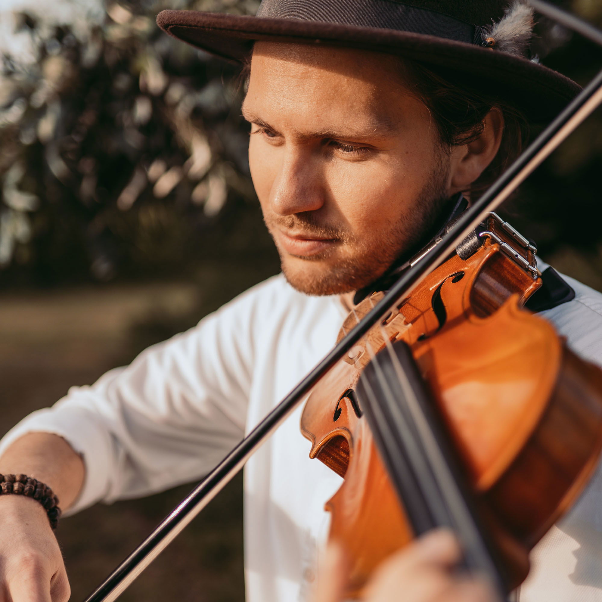 Musiker mit Hut und Geige bei einer Outdoor-Hochzeit, während er in die Musik vertieft ist.