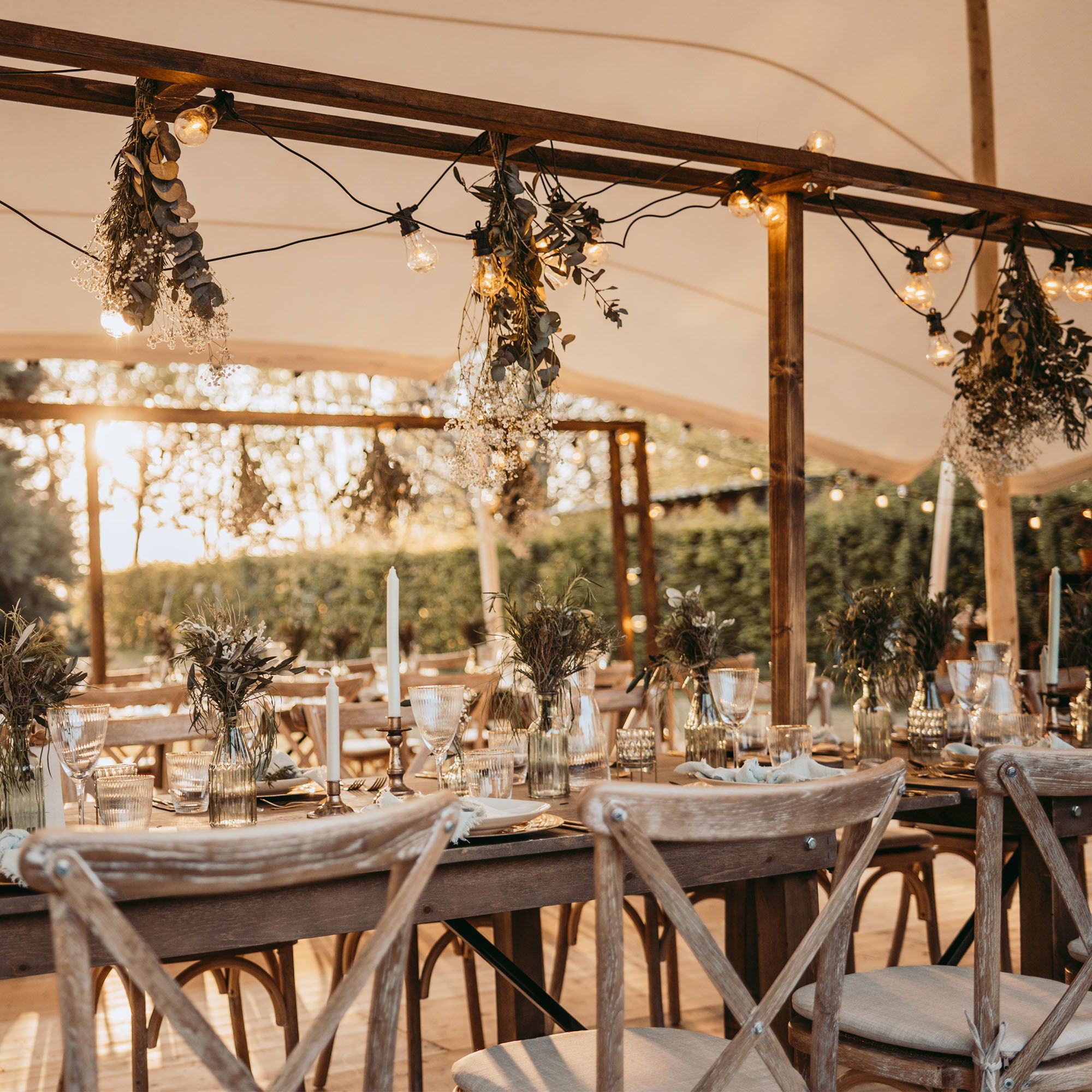 Outdoor-Hochzeitstisch mit natürlicher Pflanzen-Deko, rustikalen Stühlen und gemütlichen Lichtern, die eine romantische Atmosphäre schaffen.