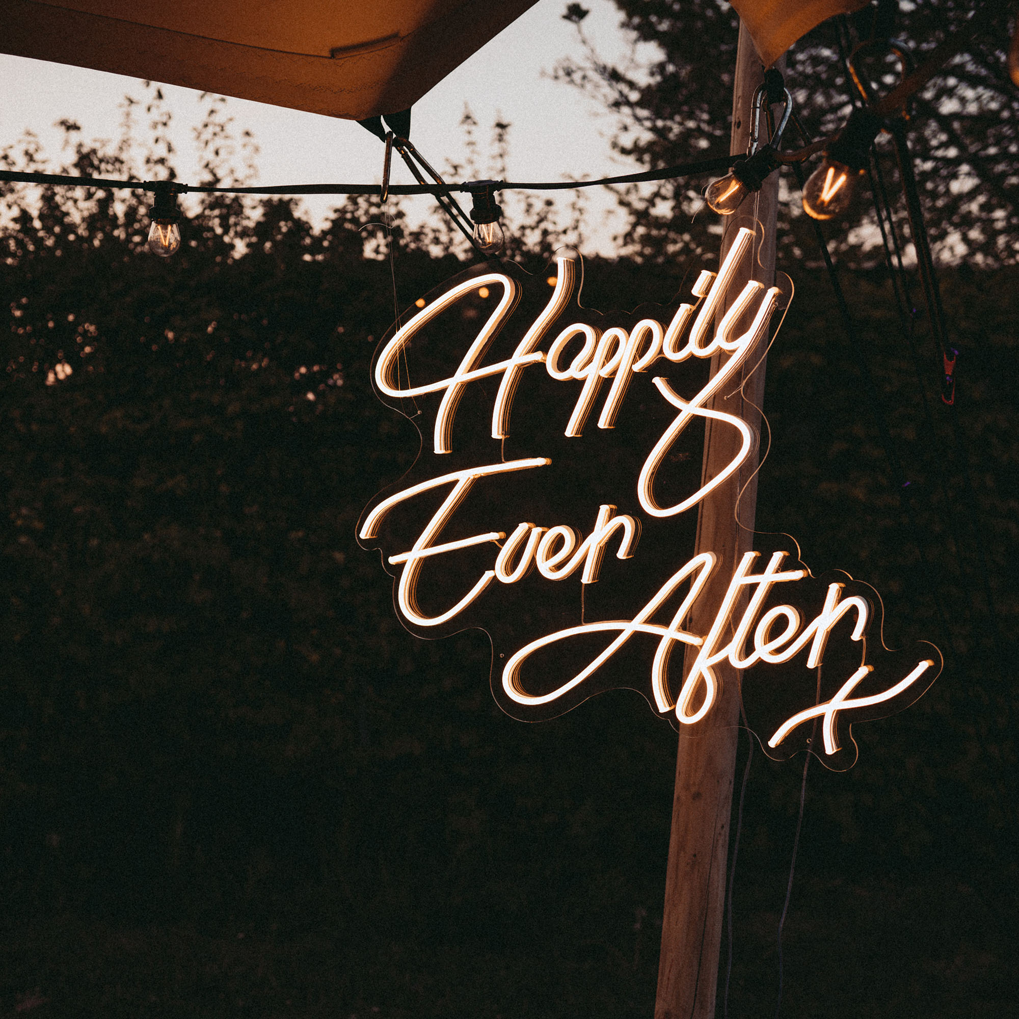 Neonschriftzug 'Happily Ever After' strahlt in der Nacht, als Teil der romantischen Dekoration einer Freiluft-Hochzeit.