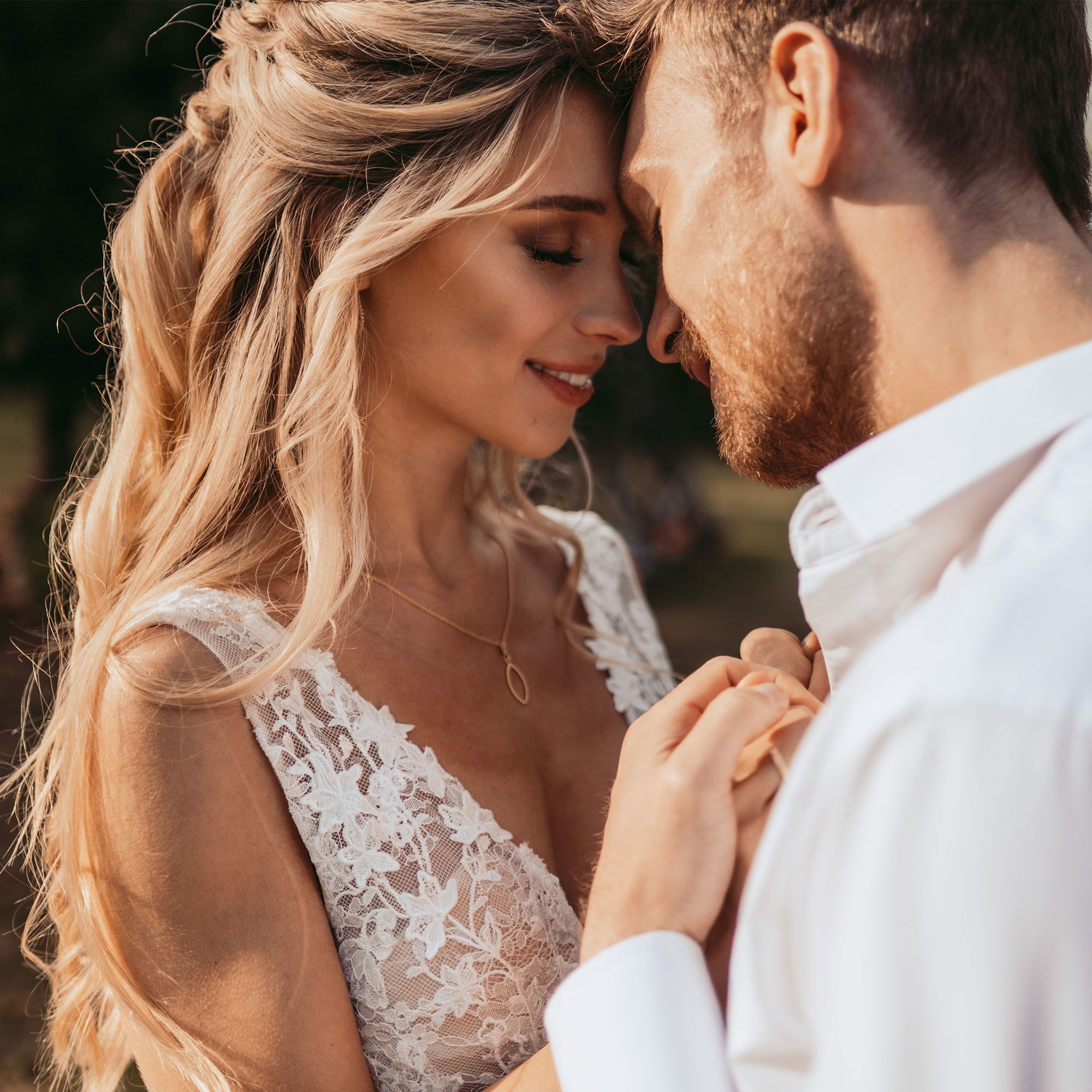 Verträumter Moment zwischen Braut und Bräutigam, die sich liebevoll zueinander neigen, während sie ihre Nähe in der sanften Abendsonne genießen.