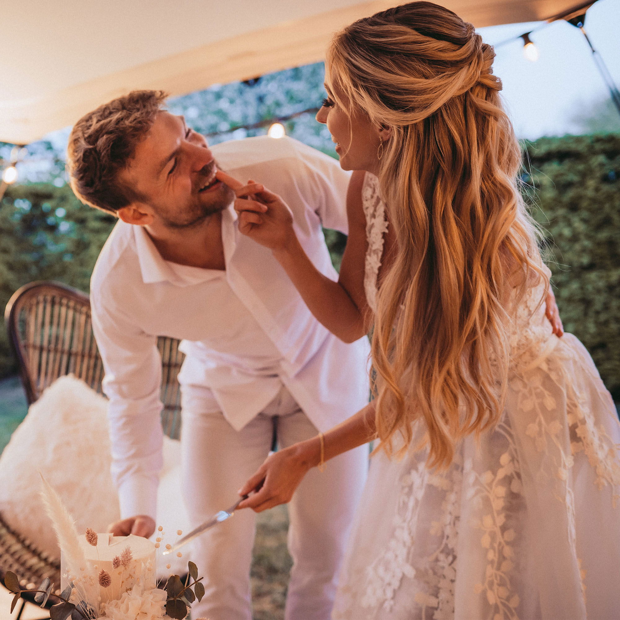 Romantischer Moment: Die Braut neckt den Bräutigam mit einem Stück Torte, während sie gemeinsam die Hochzeitstorte anschneiden.