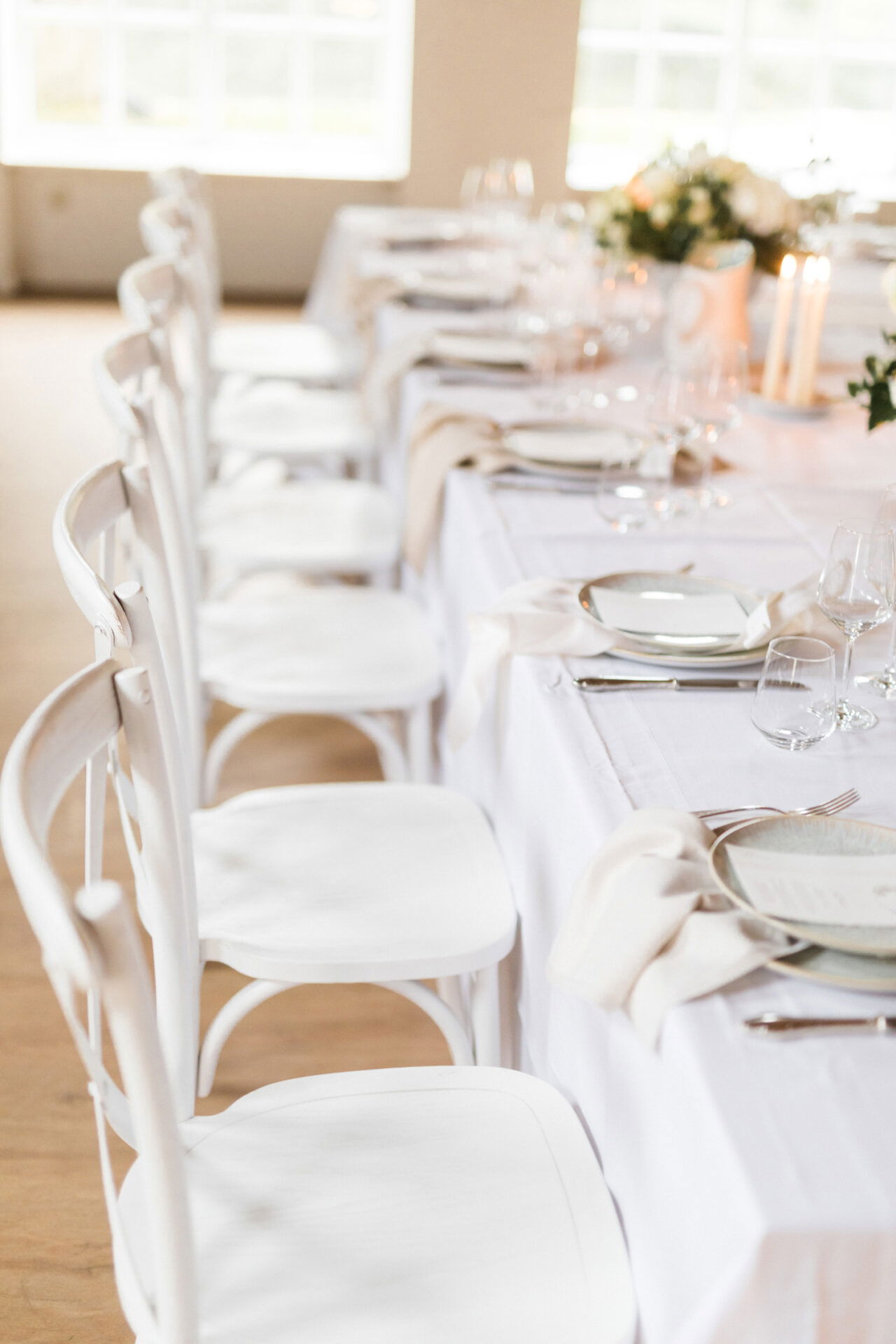 Hochzeitstafel mit weißen Stühlen und einer eleganten Tischdekoration, die eine ruhige und edle Atmosphäre für das Fest schafft.