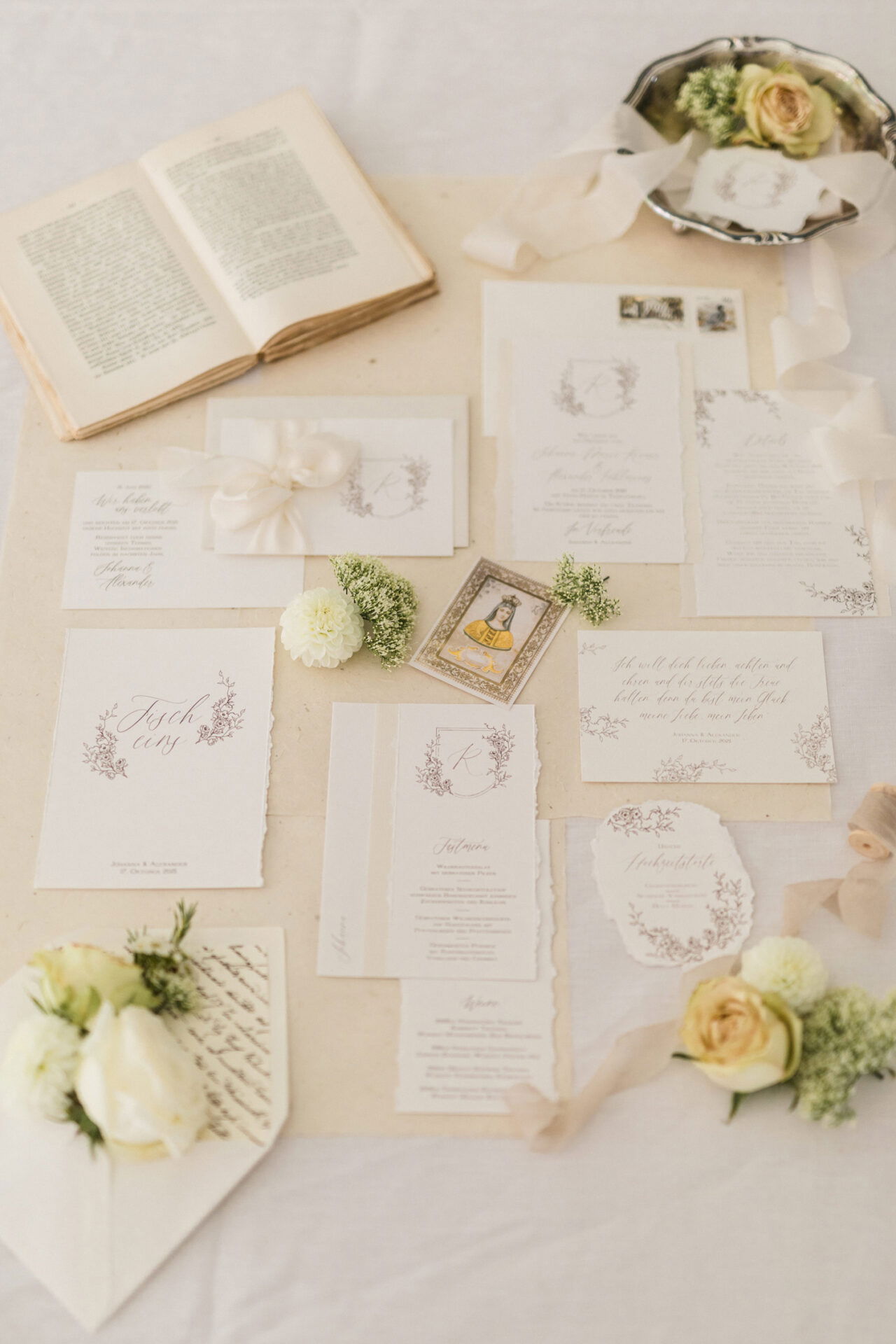 Kunstvoll gestaltete Hochzeitseinladung auf einem Leinentuch mit filigranen Blumenmotiven, umrahmt von Vintage-Accessoires und zarten Blüten.