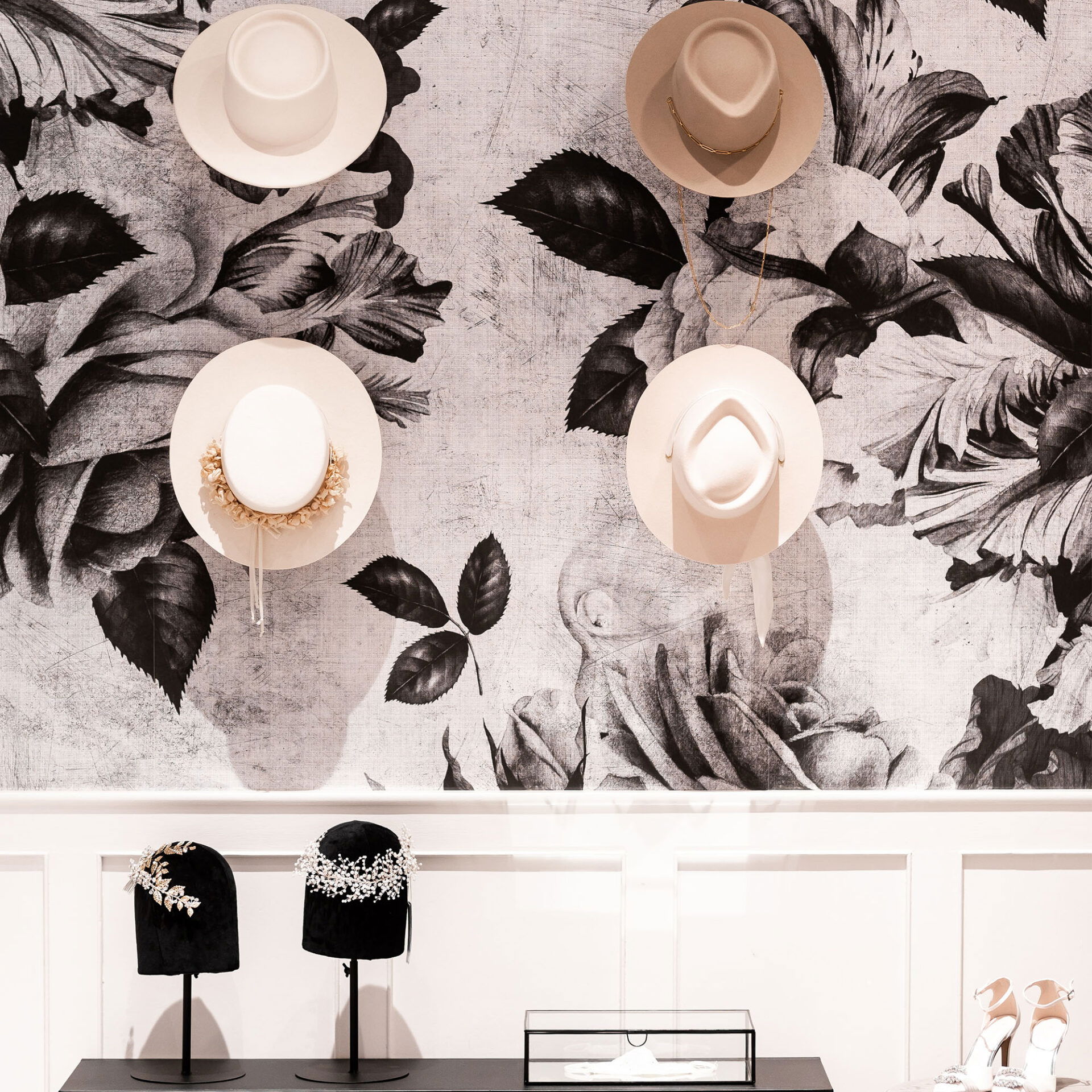 Eine kreative Präsentation von Hüten und Kopfschmuck vor einer kunstvoll dekorierten Wand im Brautmodengeschäft.