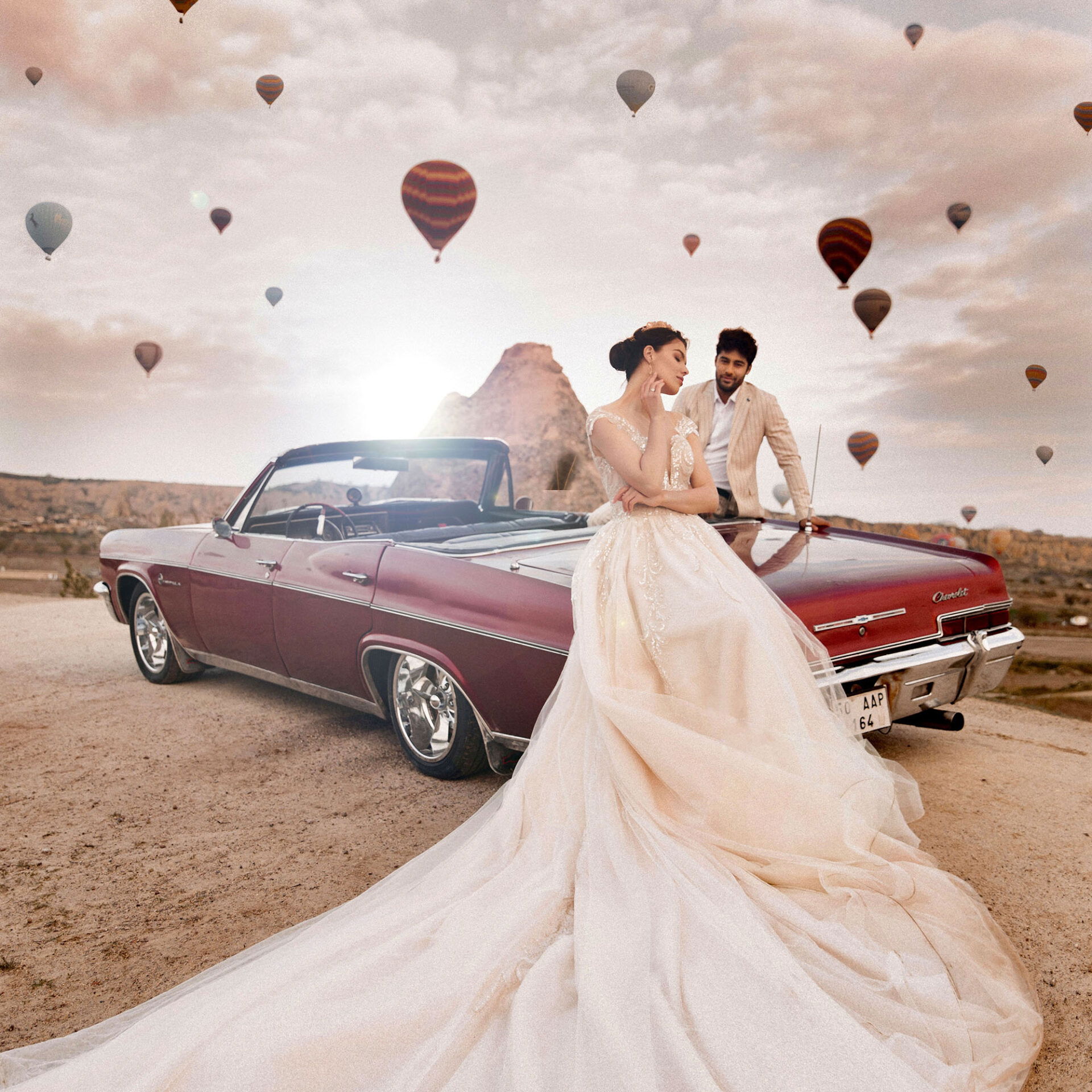 Braut und Bräutigam vor einem klassischen Cabrio, umgeben von einer malerischen Landschaft und schwebenden Heißluftballons im Hintergrund.