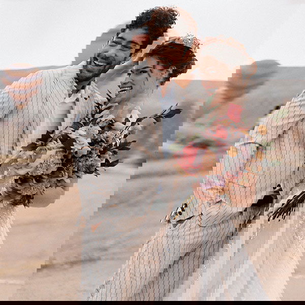 Lachendes Brautpaar mit farbenfrohem Brautstrauß, im Hintergrund Heißluftballons über der malerischen Landschaft.