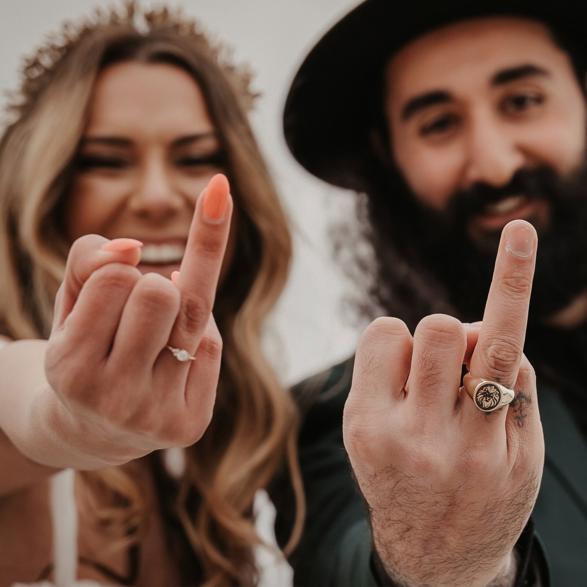 Ein frisch verheiratetes Paar zeigt humorvoll ihre Ringe in einer Nahaufnahme. Die Braut trägt einen funkelnden Verlobungsring, während der Bräutigam seinen Siegelring mit Löwenmotiv stolz zur Schau stellt.