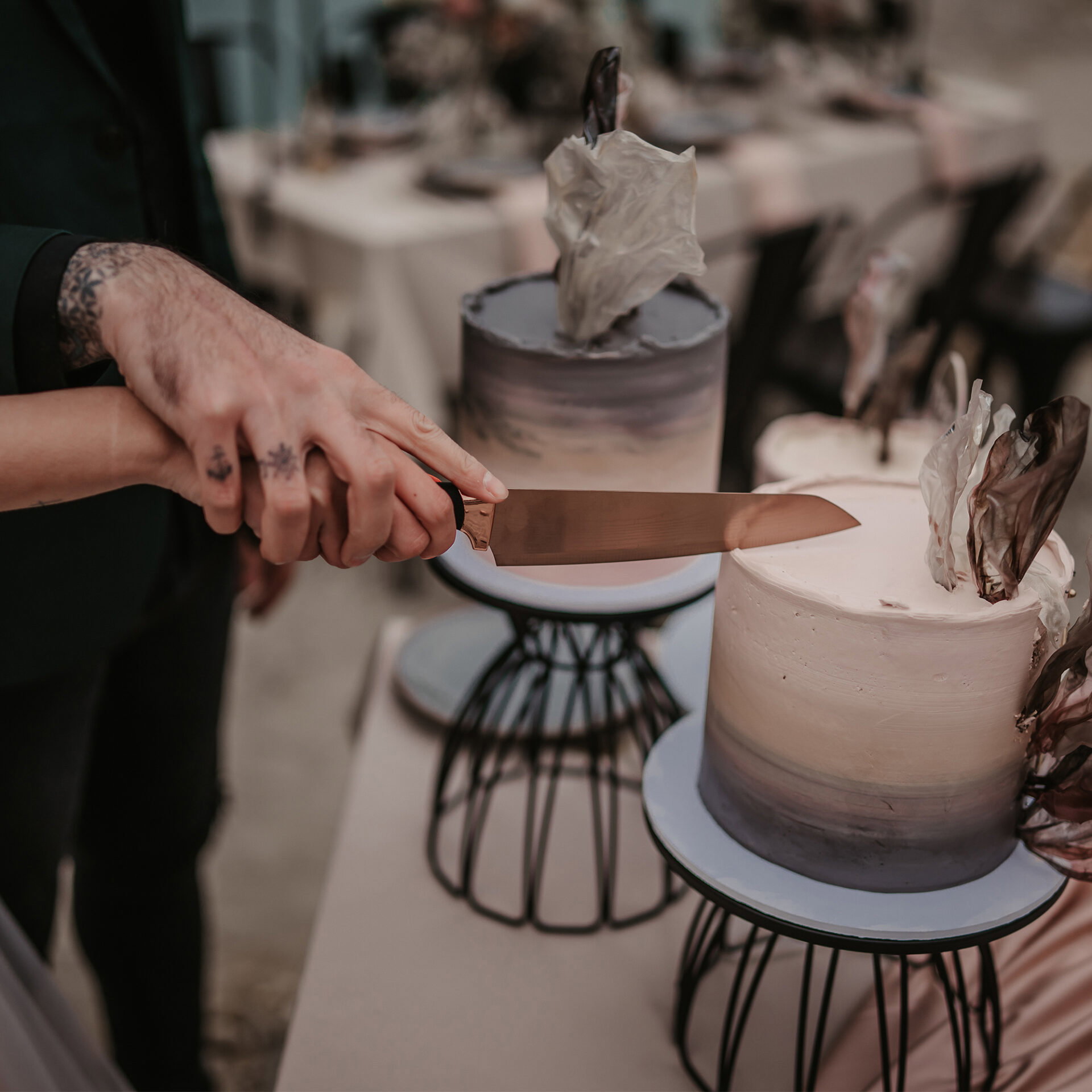 Eine Szene beim Hochzeitstortenanschnitt: Die Braut und der Bräutigam schneiden eine kunstvolle, zweistöckige Torte mit schwarzen Verzierungen und eleganten Details an.