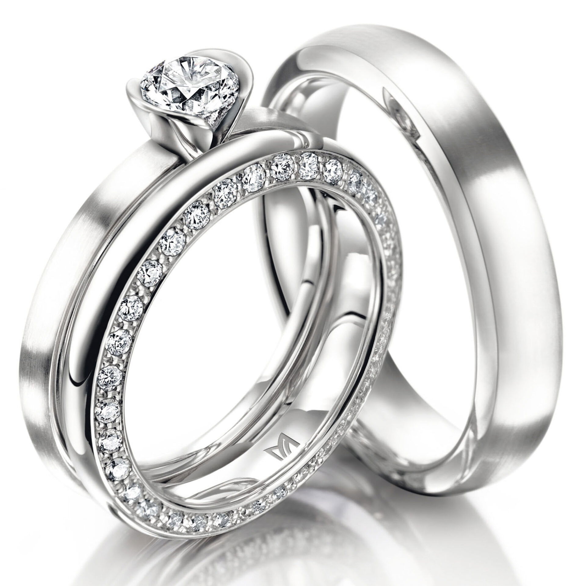 Zwei Platinringe, einer mit einem zentralen Diamanten und der andere mit einer durchgehenden Diamantreihe. Der Verlobungsring besitzt eine auffällige Fassung, die den Diamanten zur Geltung bringt.