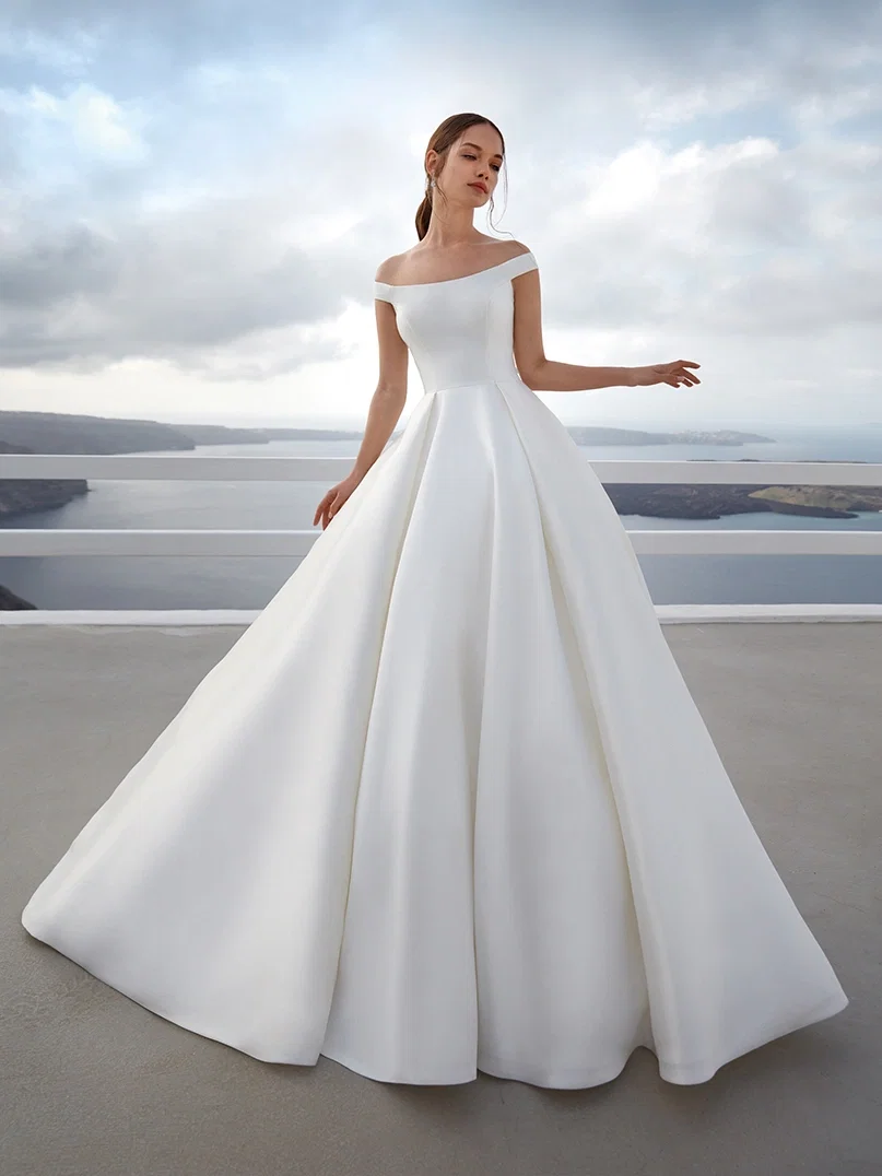 Modell in einem eleganten, schulterfreien Ballkleid mit voluminösem Rock, posiert auf einer Terrasse mit Blick auf das Meer, während Wolken den Himmel bedecken.