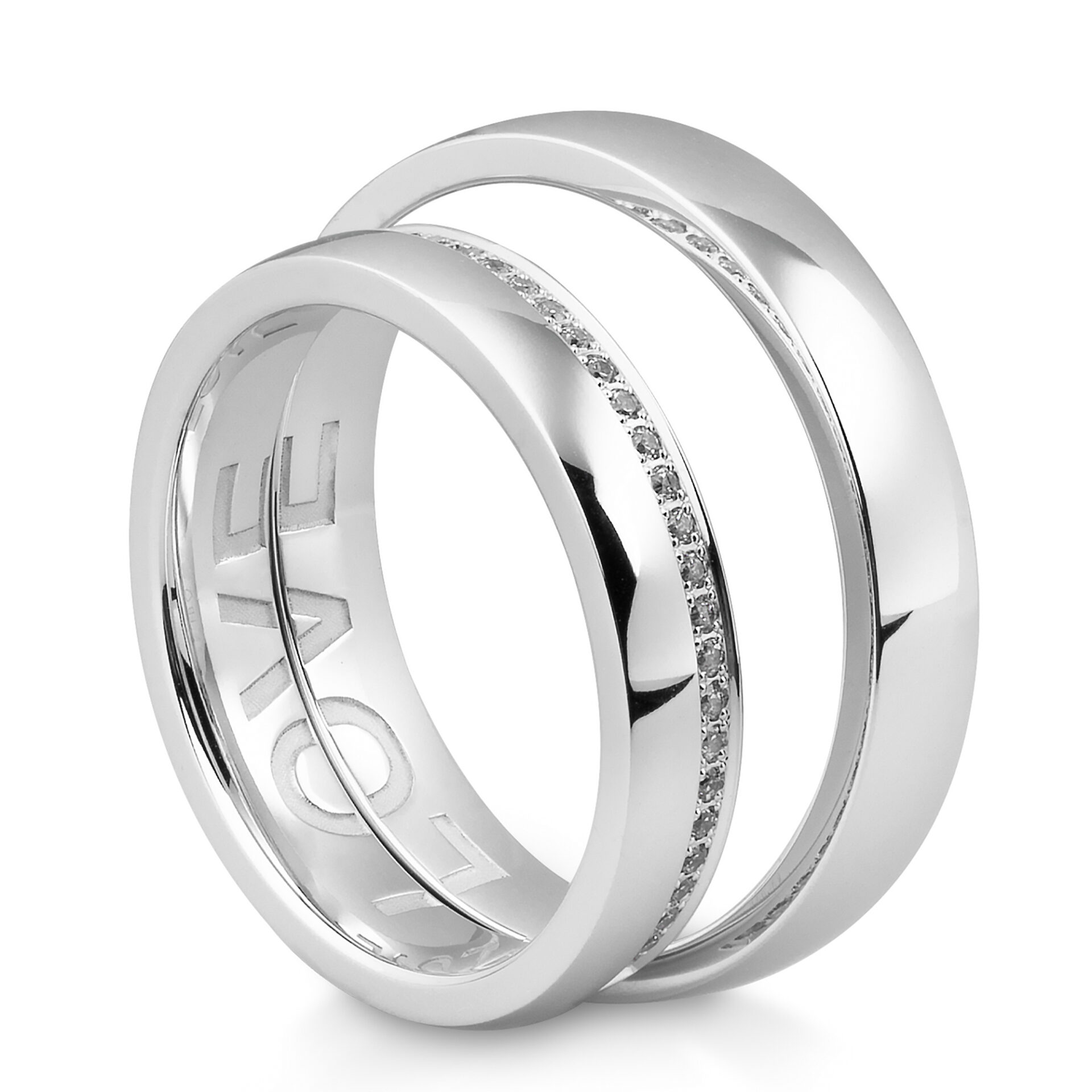 Ein Paar schlichter und funkelnder Weißgoldringe. Einer der Ringe hat eine schmale Diamantreihe, während der andere ein graviertes "LOVE" auf der Innenseite trägt, sichtbar durch den offenen Winkel.