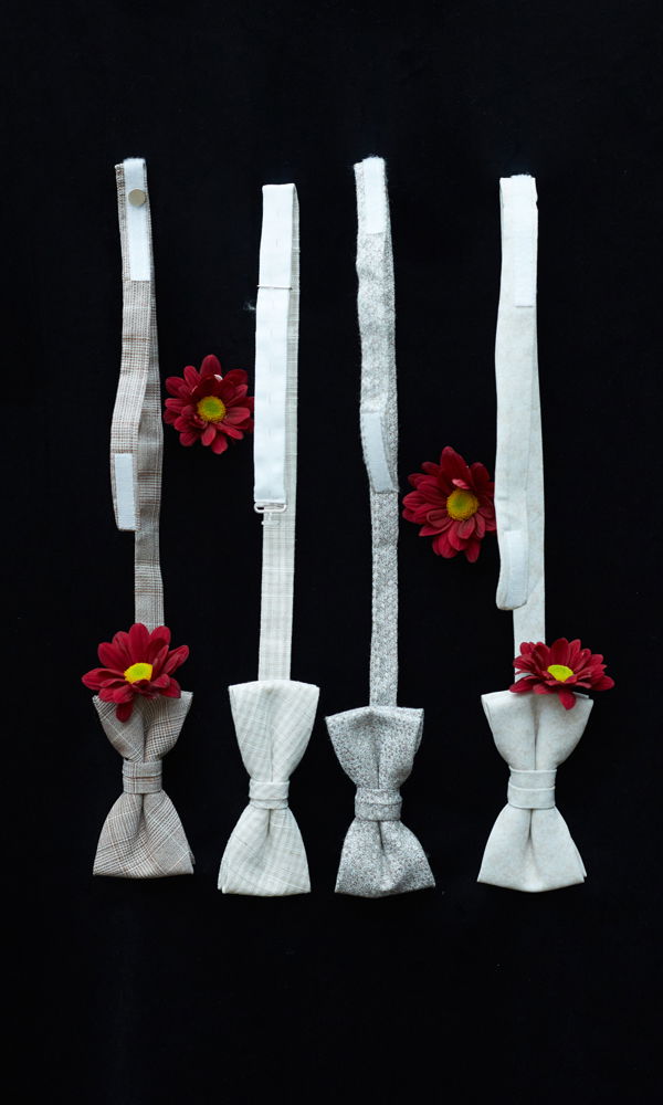 Eine Reihe von vier unterschiedlichen Fliegen, jede mit einer roten Blüte geschmückt, präsentiert auf schwarzem Untergrund.