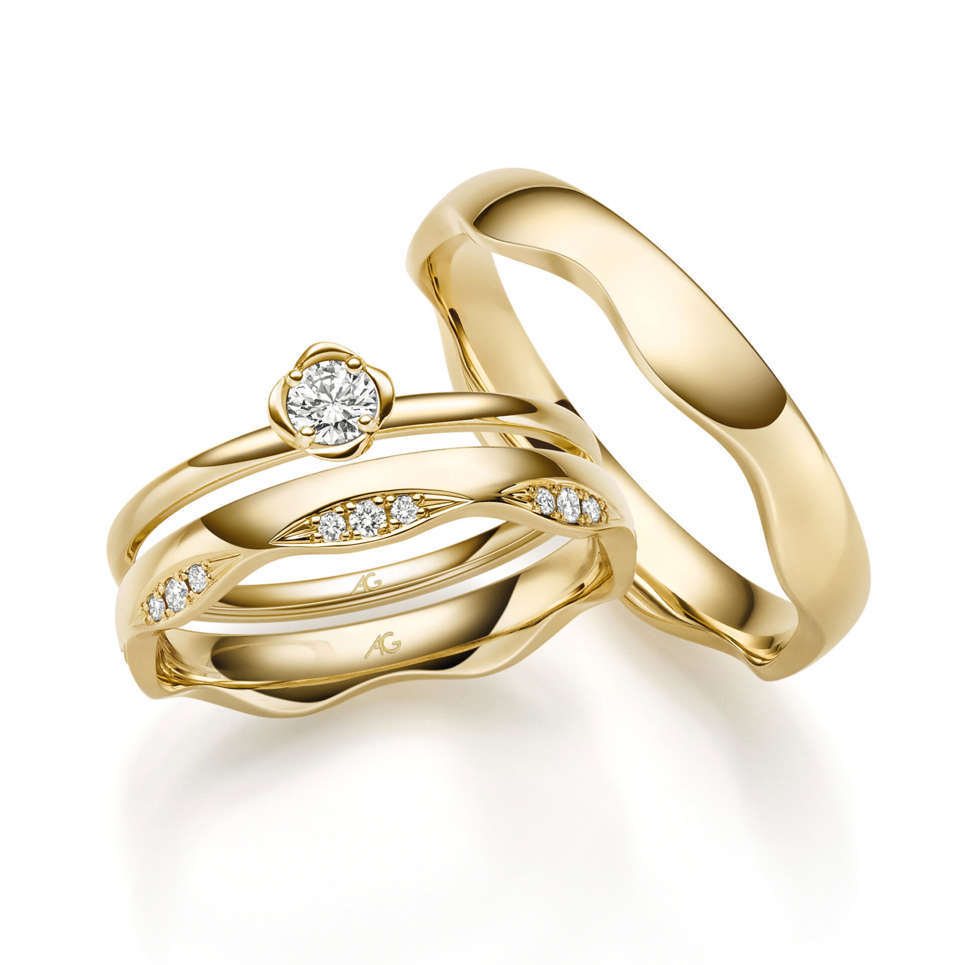 Drei luxuriöse gelbgoldene Ringe, von denen einer einen großen Diamanten in der Mitte hat und die anderen beiden mit Diamanten besetzt sind. Ein schlichter Ehering vervollständigt das Set.