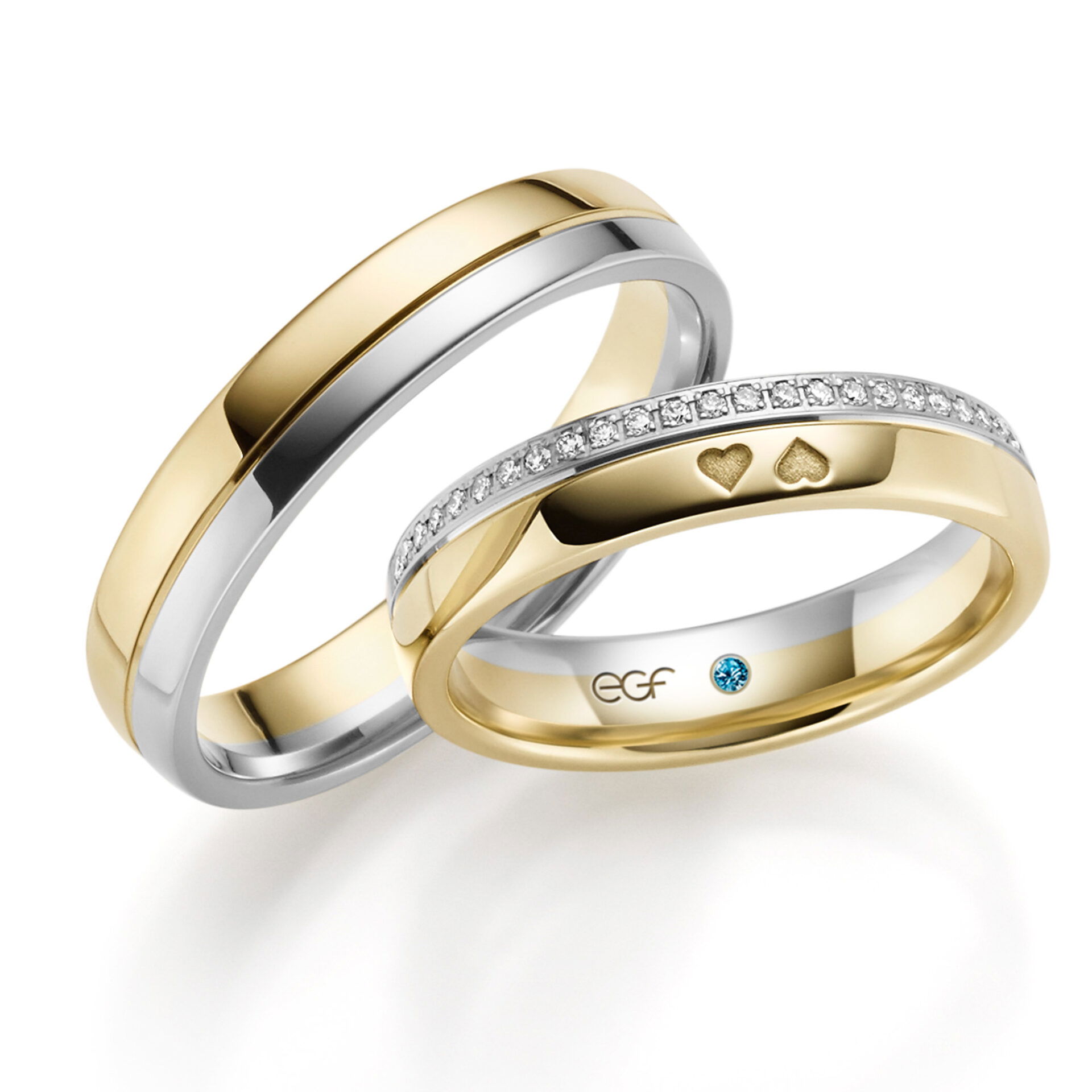 Zwei stilvolle Eheringe, die aus Gelbgold und Weißgold gefertigt sind. Der Ring der Braut ist mit funkelnden Diamanten und Herzgravuren verziert, während der schlichte Ring des Bräutigams einen minimalistischen Look hat.