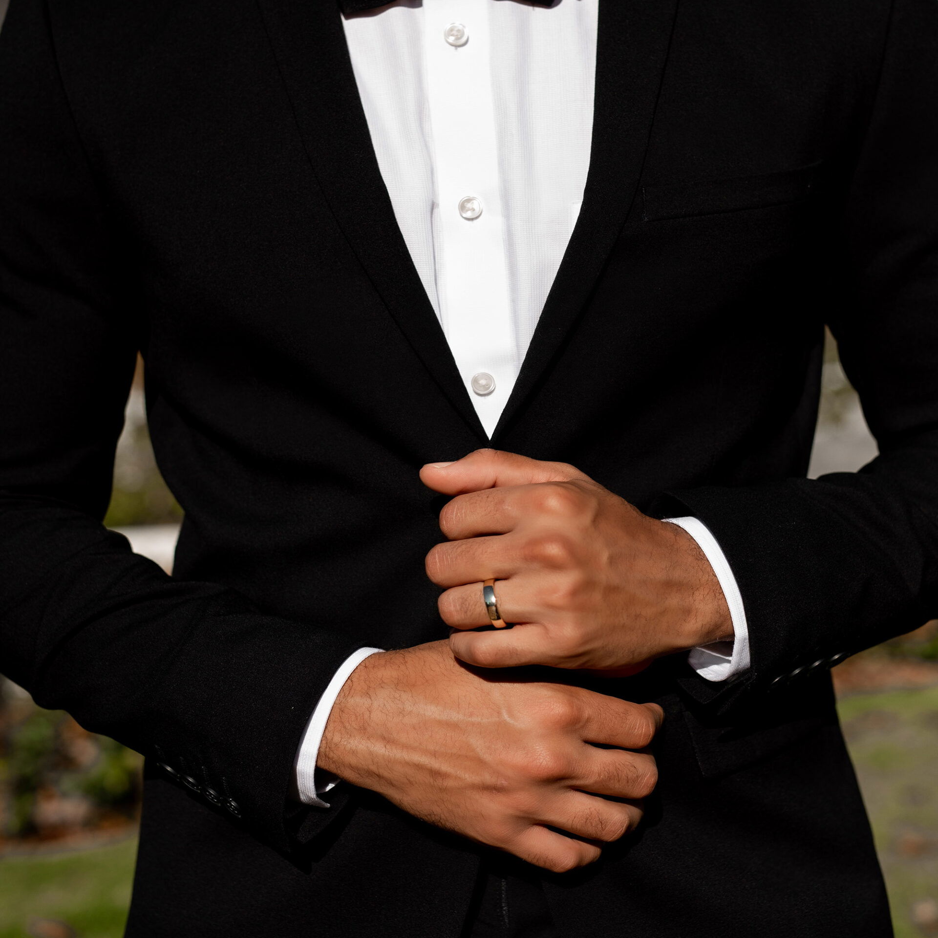 Ein eleganter Bräutigam in klassischem Schwarz mit Fliege und weißem Hemd. Er zeigt stolz seinen Ehering und strahlt Selbstbewusstsein aus.