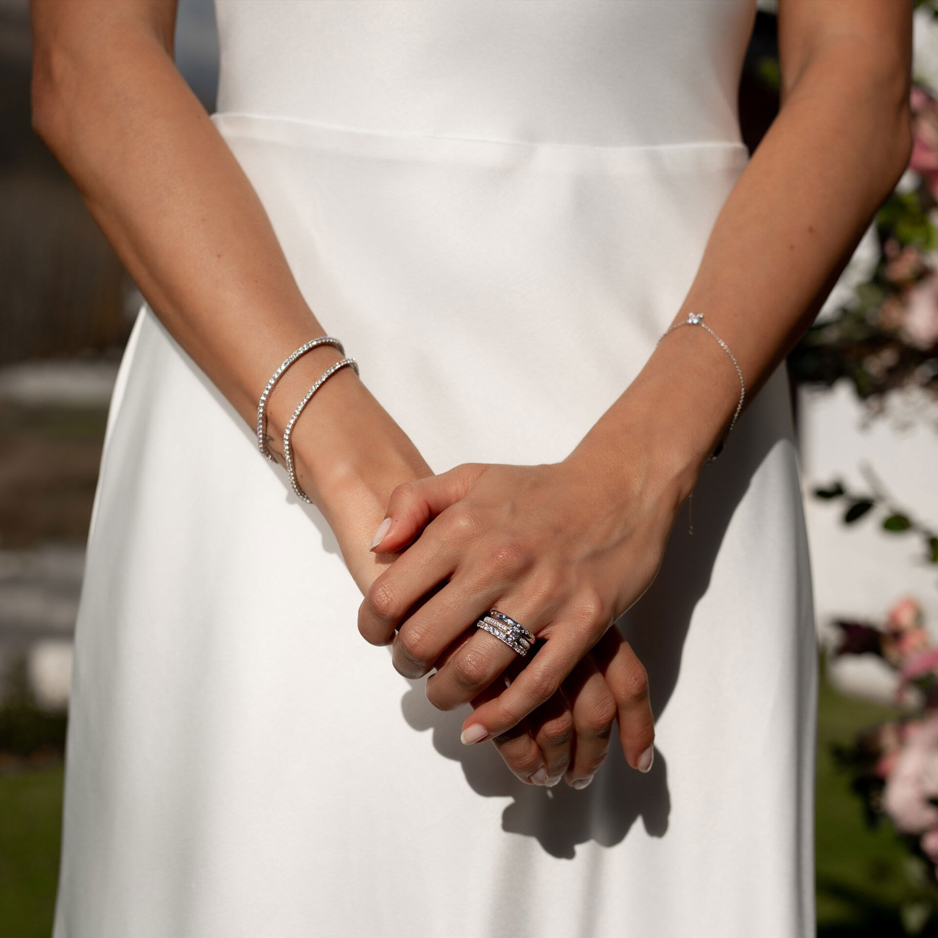 Die Braut trägt ein minimalistisches Hochzeitskleid und präsentiert ihren funkelnden Ehering, ergänzt durch zarte, silberne Armbänder an ihrem Handgelenk.