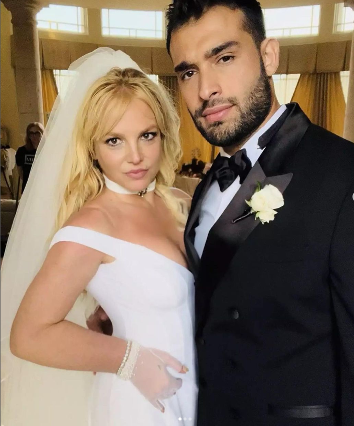 Braut mit langen blonden Haaren und einem weißen Brautkleid neben dem Bräutigam in einem Smoking mit Ansteckblume, beide posieren zusammen für ein Hochzeitsbild.