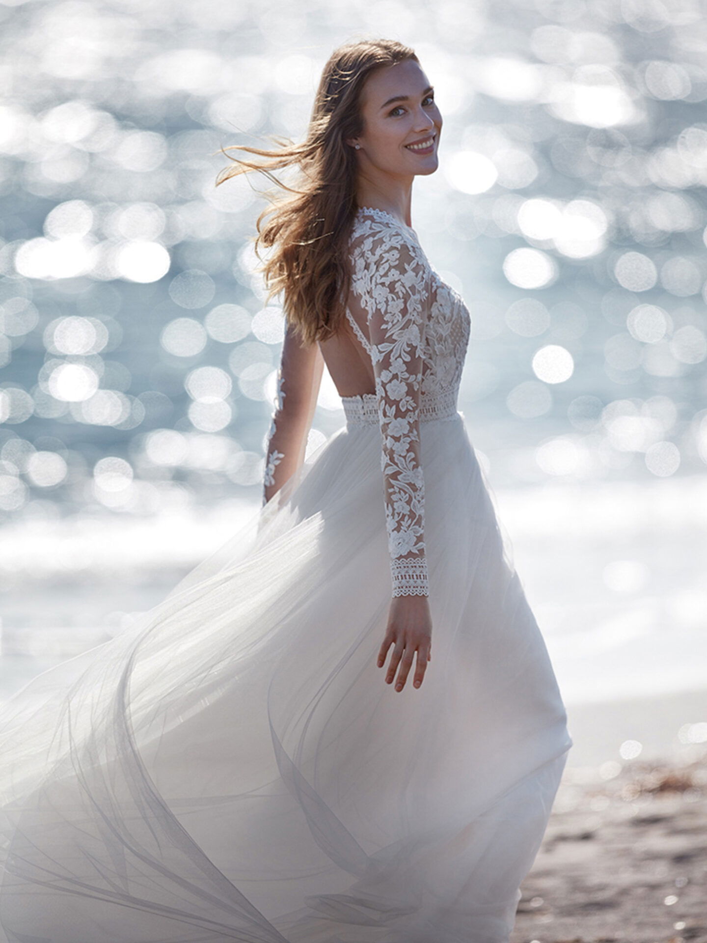 Braut im Hochzeitskleid mit Spitzenärmeln am Strand laufend