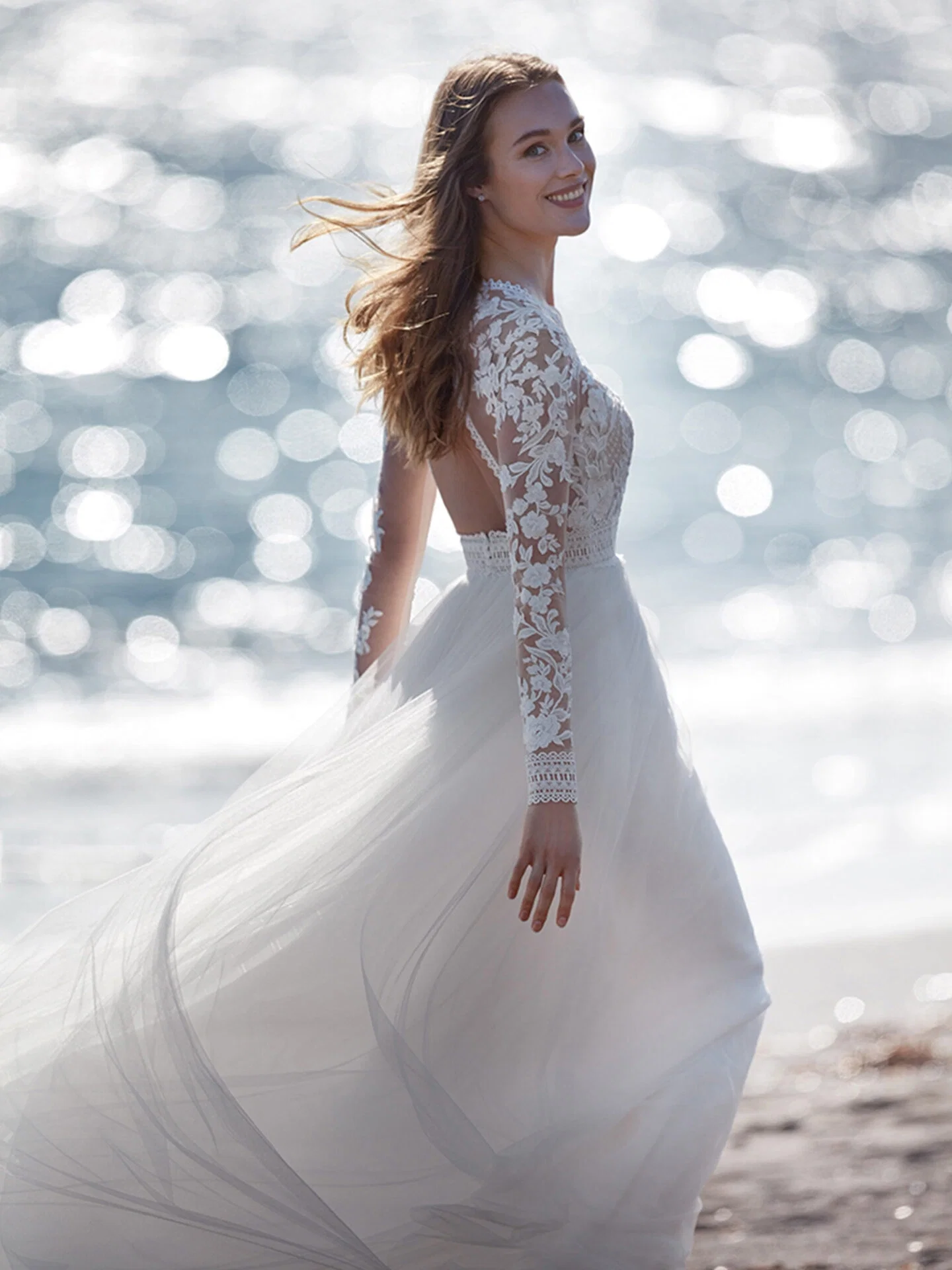 Braut im Hochzeitskleid mit Spitzenärmeln am Strand laufend