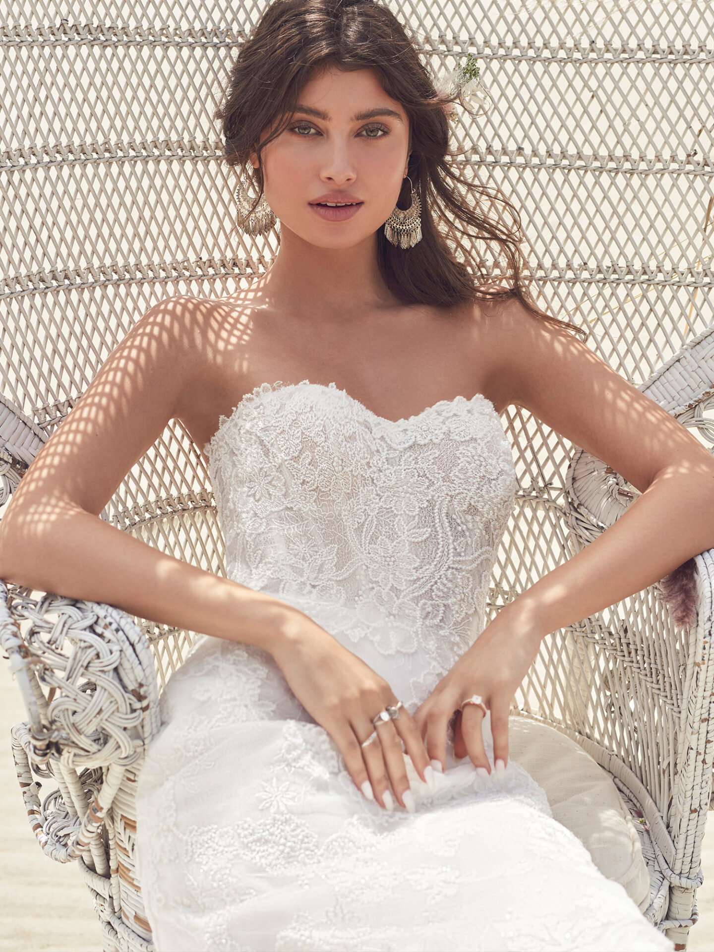 Braut im Hochzeitskleid aus Spitze am Strand in einem Stuhl sitzend