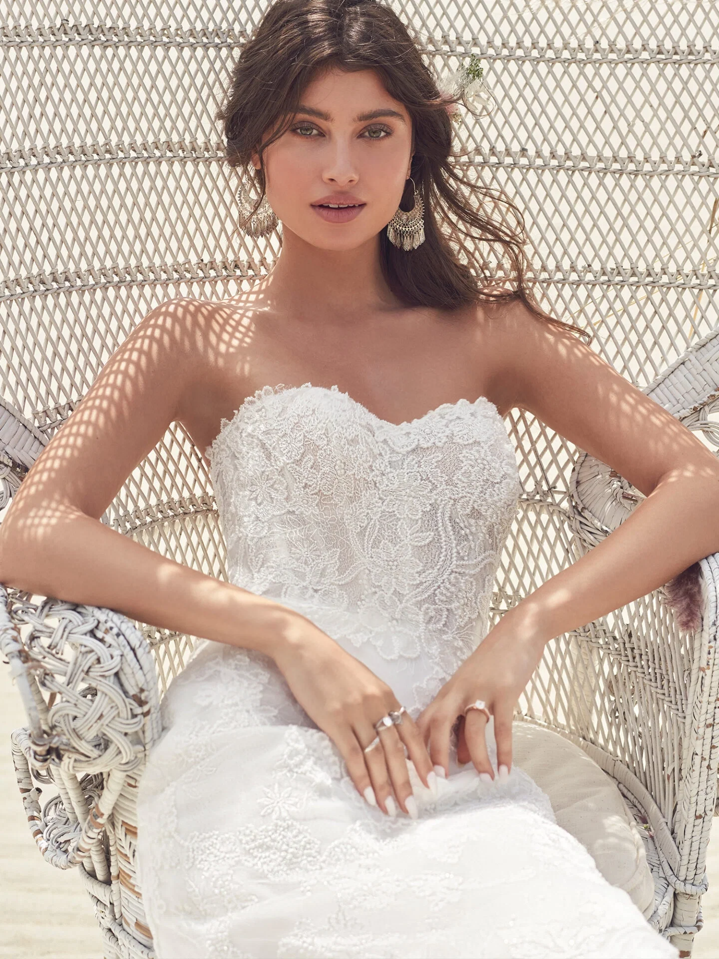 Braut im Hochzeitskleid aus Spitze am Strand in einem Stuhl sitzend