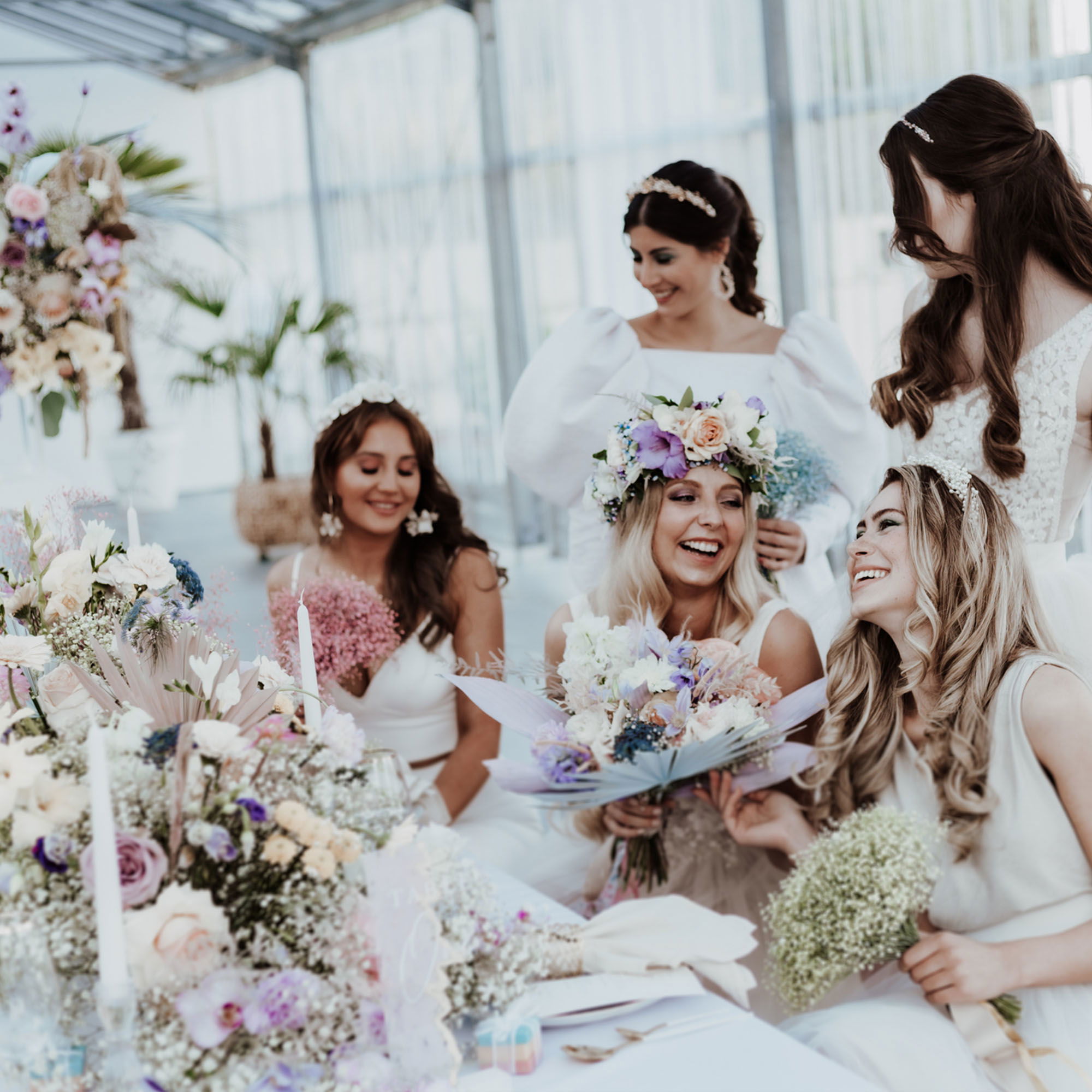 Eine Gruppe von Frauen, gekleidet in stilvolle Hochzeitskleider, sitzt um einen Tisch mit blumigen Dekorationen und unterhält sich lachend.