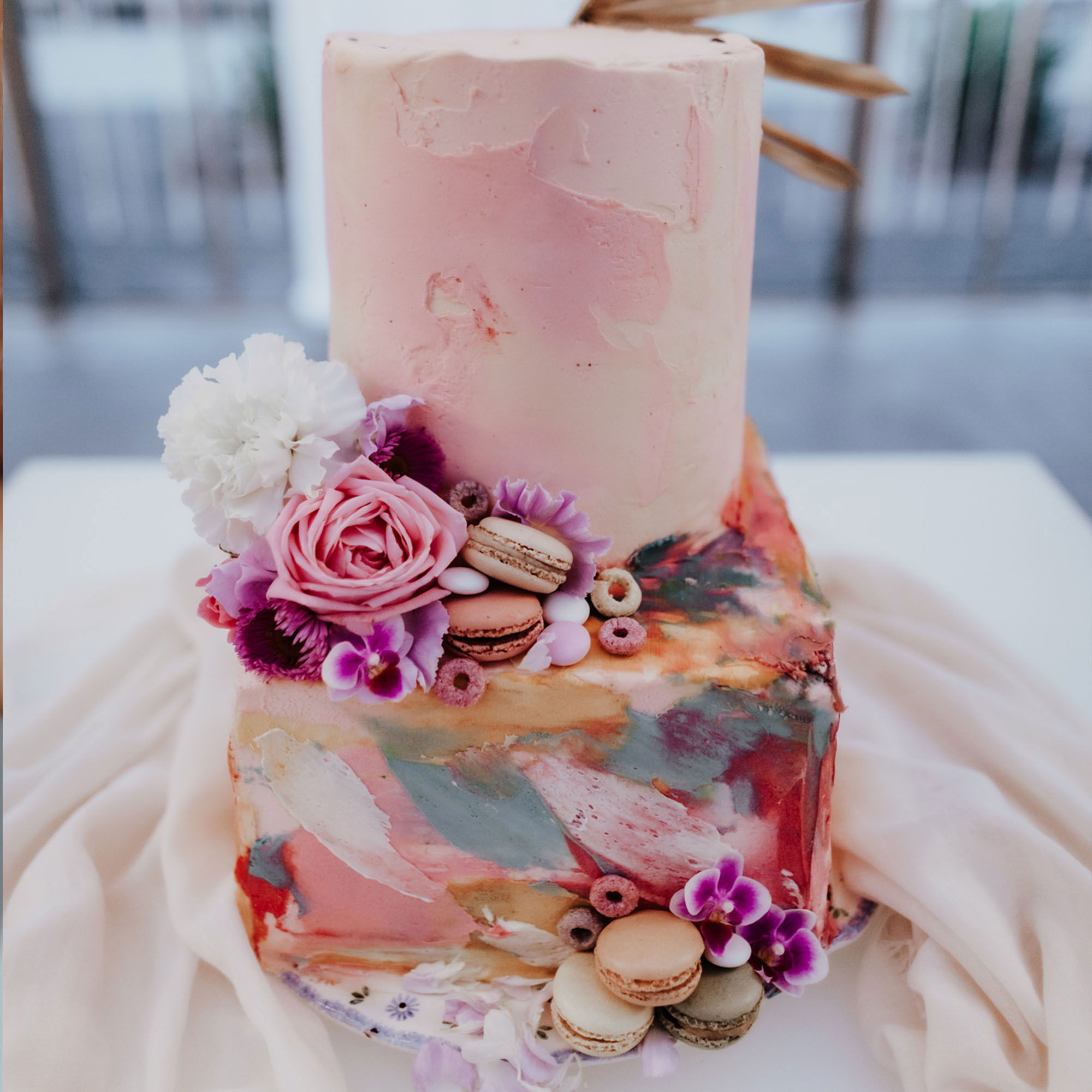 Handgemachte Hochzeitstorte in einem künstlerischen Design, dekoriert mit Blumen und süßen Macarons in verschiedenen Farben, die den Tortenrand zieren.
