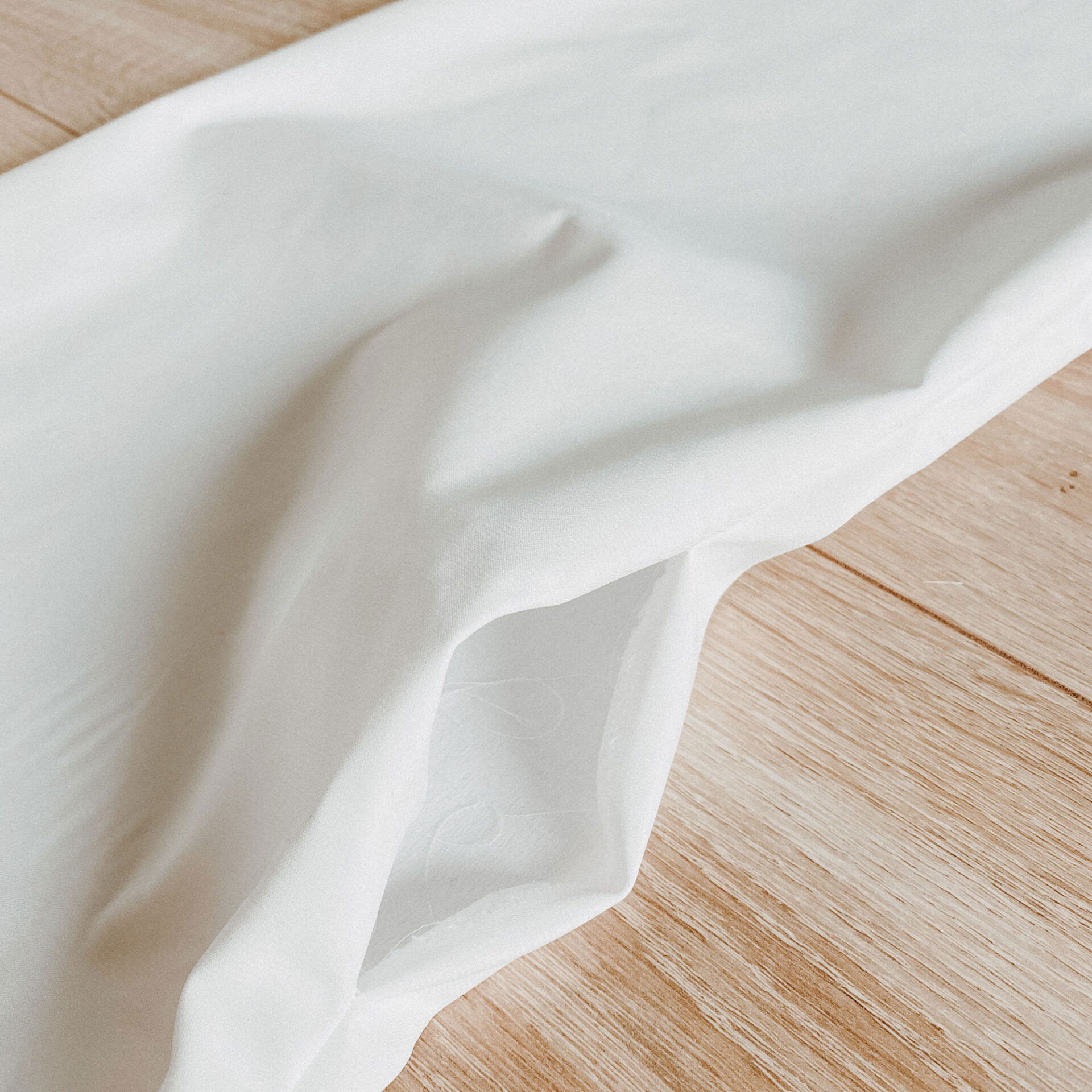 Ein weicher, weißer Stoff ist lose auf einem Holzboden ausgelegt, und seine feine Textur und Falten sind gut zu erkennen.