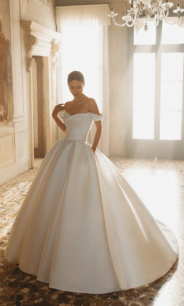 Elegant besticktes Kleid mit transparenter Spitze und dramatischem Volumen, ideal für Märchenhochzeiten.