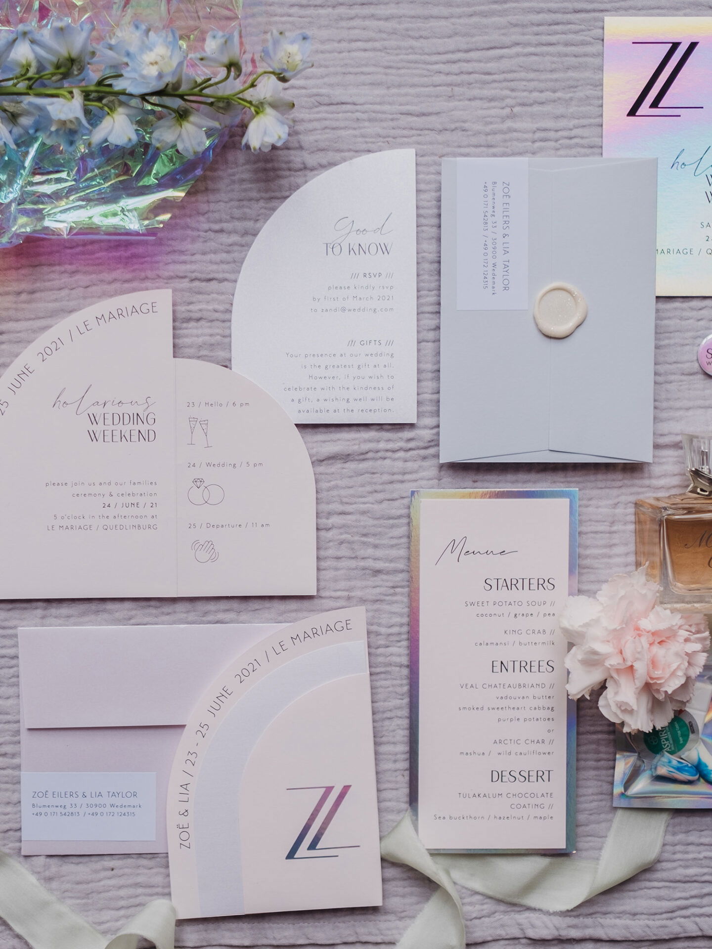 Mehrere Hochzeitseinladungen und Karten, darunter Menüs und RSVP-Informationen, sind auf einer weichen, strukturierten Unterlage arrangiert. Das Design ist minimalistisch und elegant, begleitet von zarten Blumen und einem sanft schimmernden, modernen Farbschema.