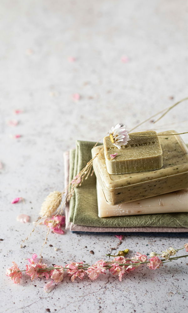 Detailaufnahme von Seifenstücken auf gefalteten Stoffen. Getrocknete Blumen und dezente Farben schaffen eine entspannte, natürliche Atmosphäre.