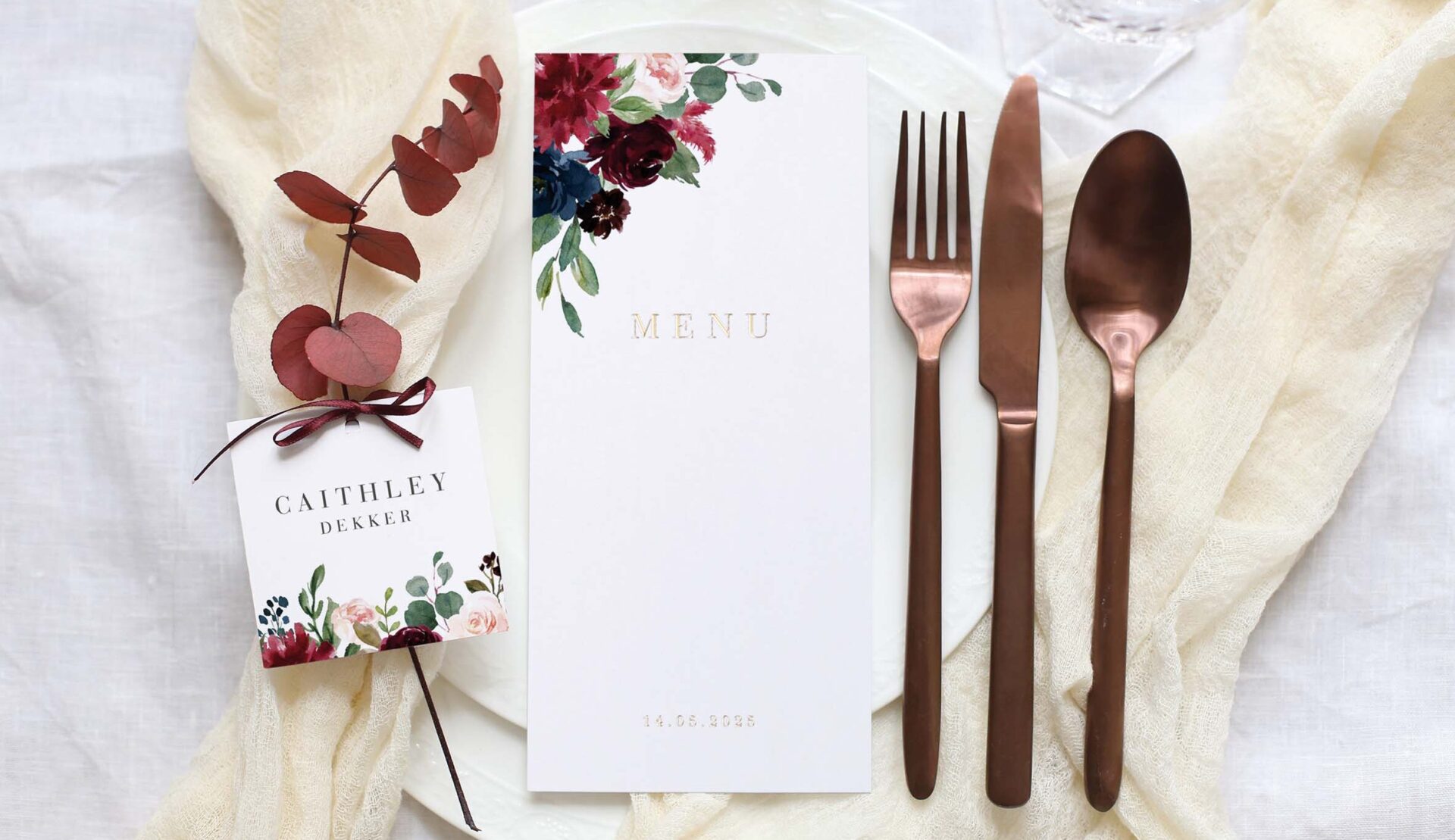 Fein gedeckter Hochzeitstisch mit floralem Thema, einer Menükarte, personalisierter Platzkarte und stilvollem Kupferbesteck.
