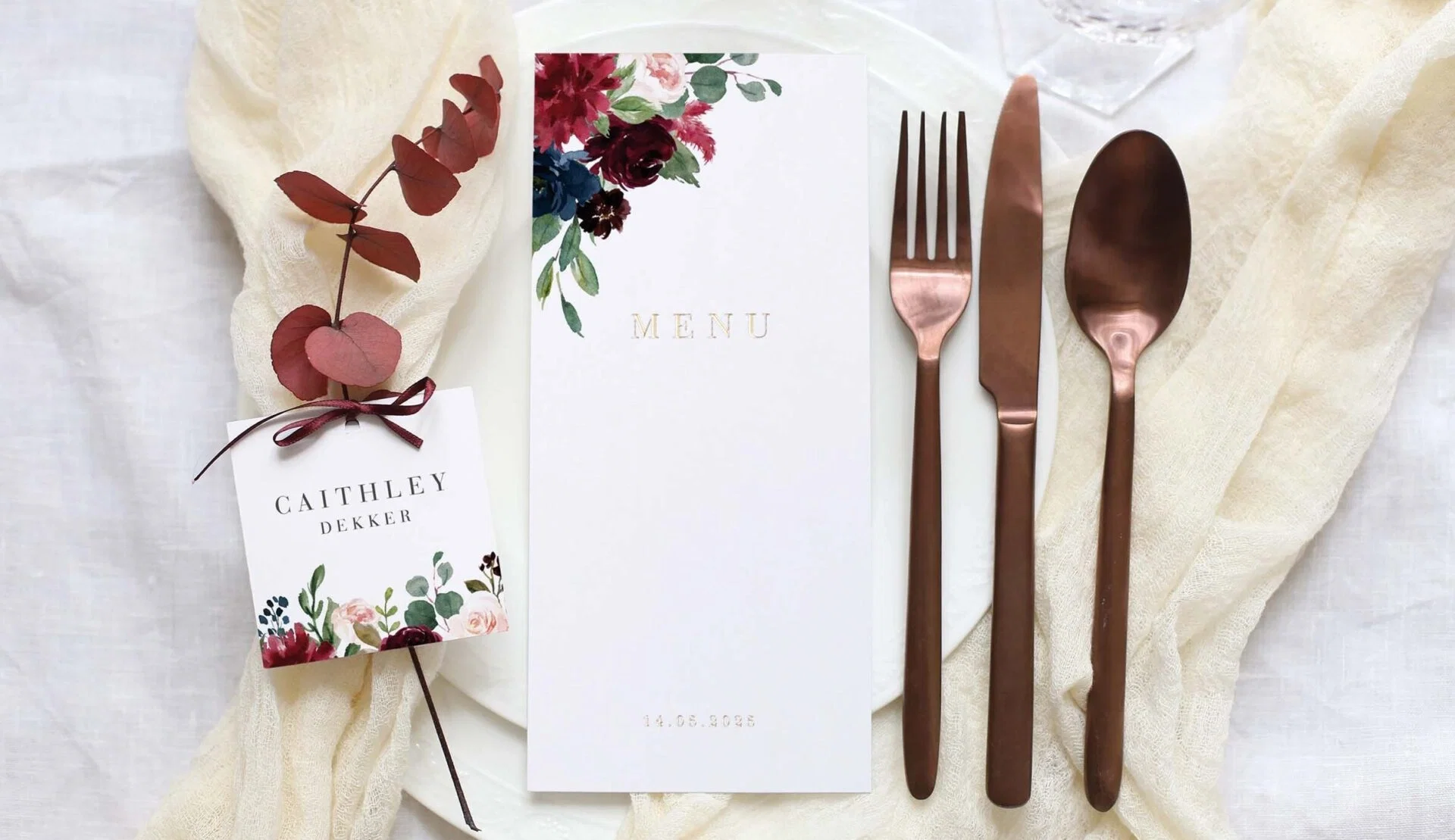 Fein gedeckter Hochzeitstisch mit floralem Thema, einer Menükarte, personalisierter Platzkarte und stilvollem Kupferbesteck.