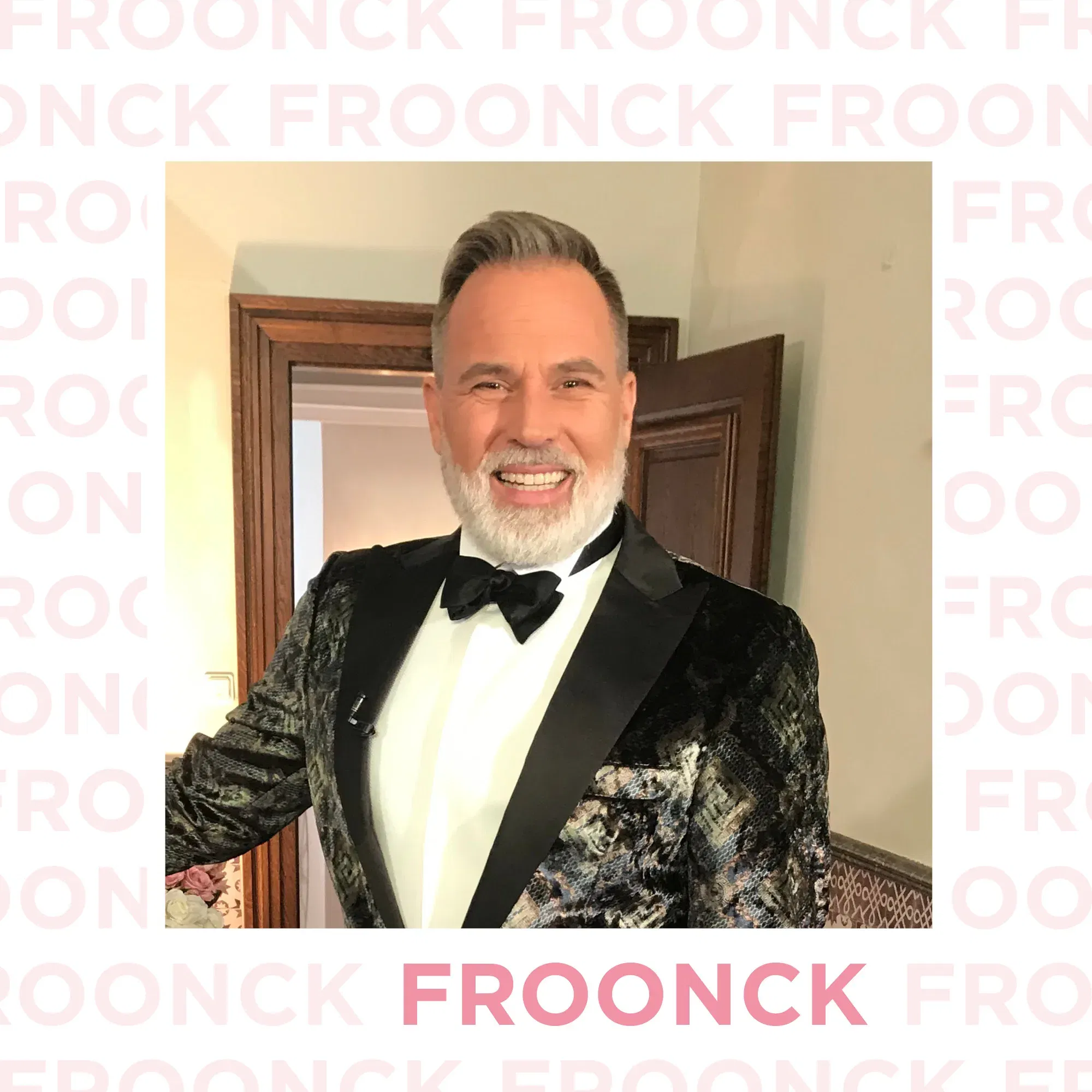 Froonck, gekleidet in einem festlichen schwarzen Smoking, lächelt in einem elegant dekorierten Raum. Sein Outfit und sein strahlendes Lächeln verleihen ihm einen professionellen und charismatischen Look.