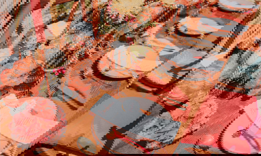 Festlich gedeckter Hochzeitstisch mit Blumendekoration in kräftigem Orange und Gelb, modernen Kerzenhaltern, Menüpapeterie und farblich abgestimmten Stuhlkissen.