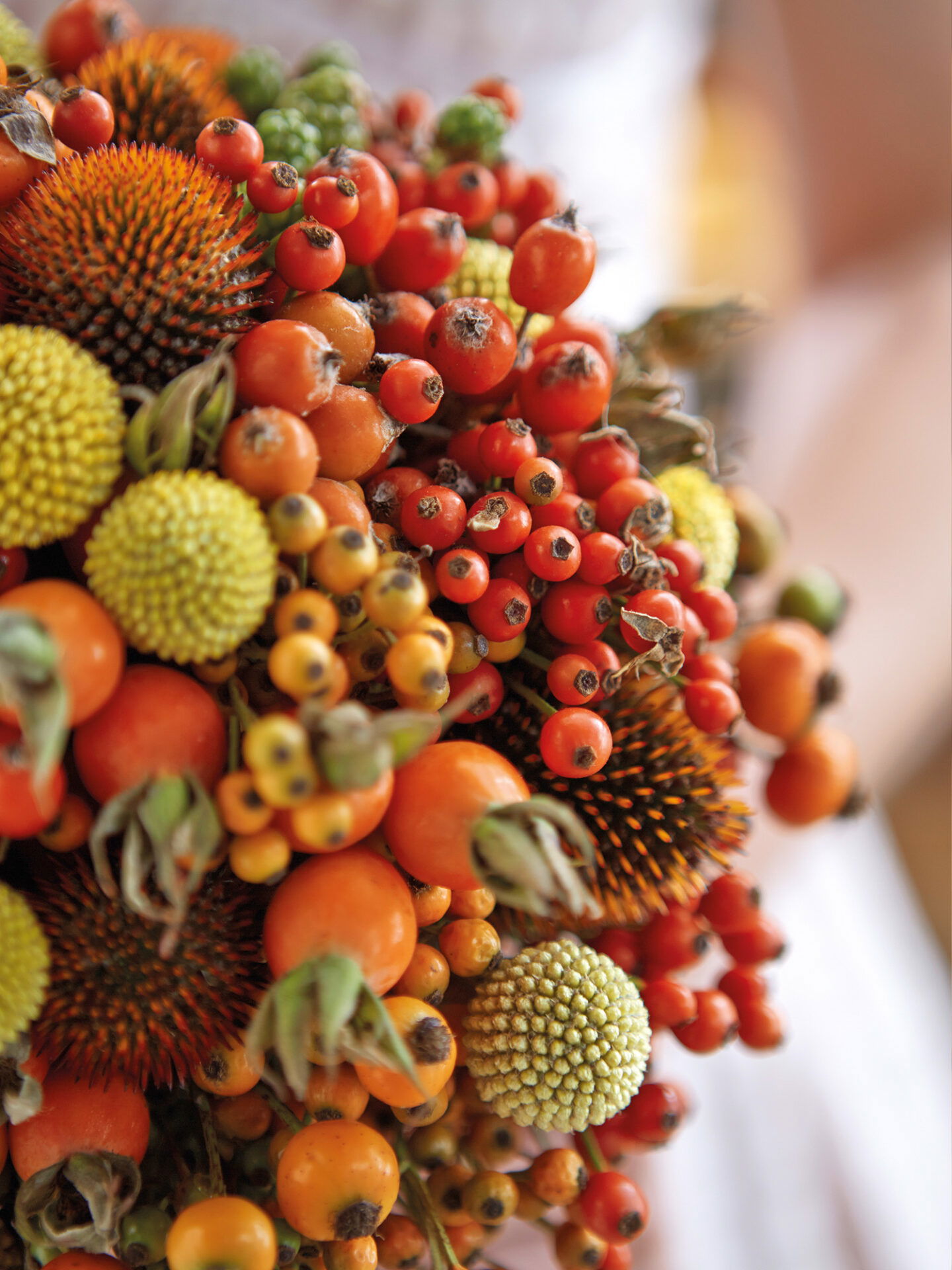 Ein kreativer Brautstrauß bestehend aus verschiedenfarbigen Beeren und Früchten in Orange- und Grüntönen, ideal für herbstliche Feierlichkeiten.