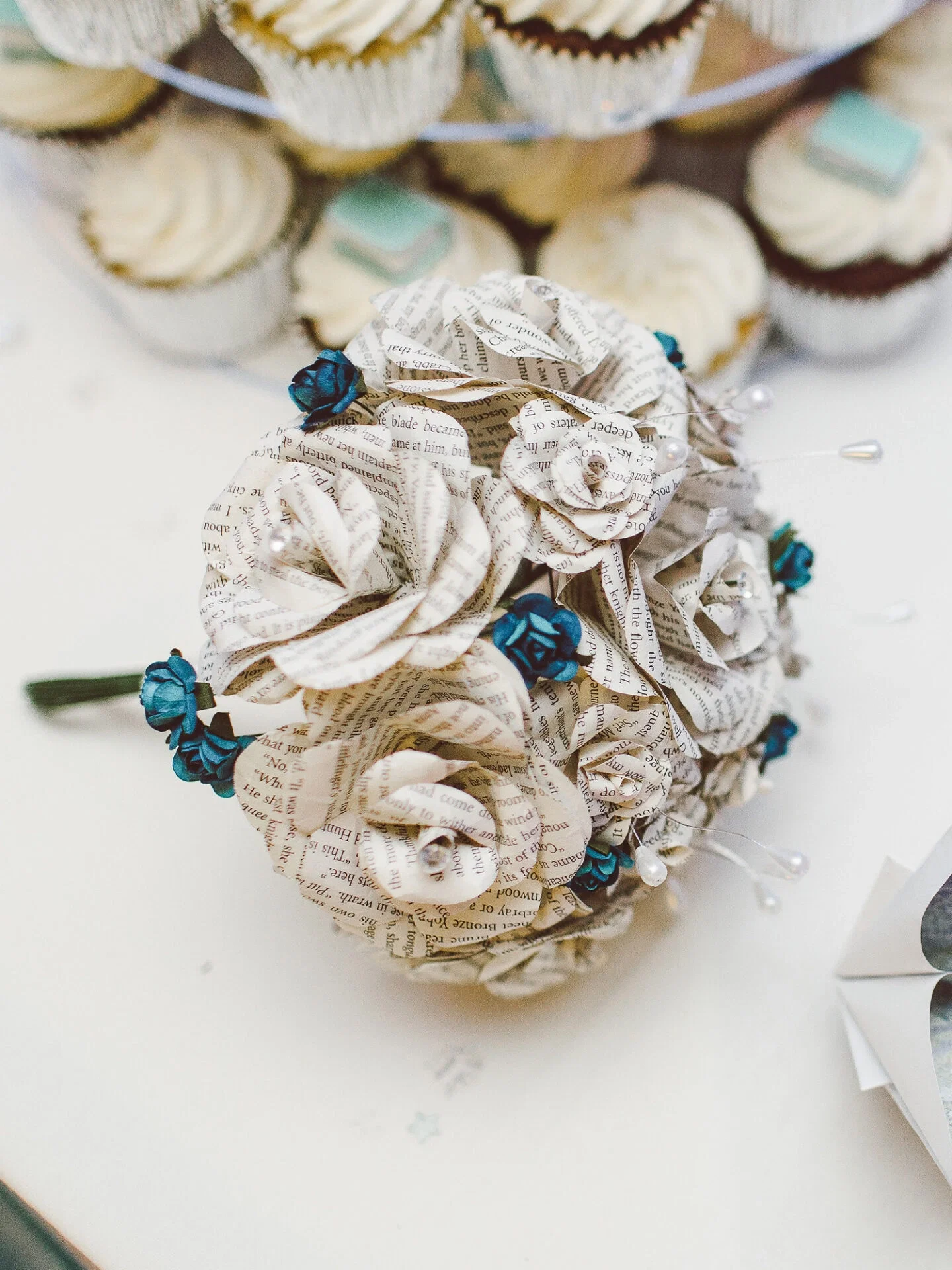 Detailaufnahme eines kunstvoll gestalteten Brautstraußes aus Papierrosen, kombiniert mit blauen Blüten und feinen Perlen, ideal für eine kreative Hochzeit.
