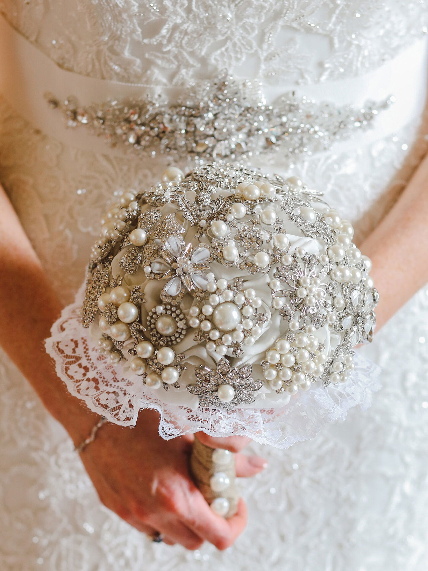 Brautstrauß mit funkelnden Perlen und Strass-Elementen, gehalten von der Braut in einem filigran bestickten Hochzeitskleid.