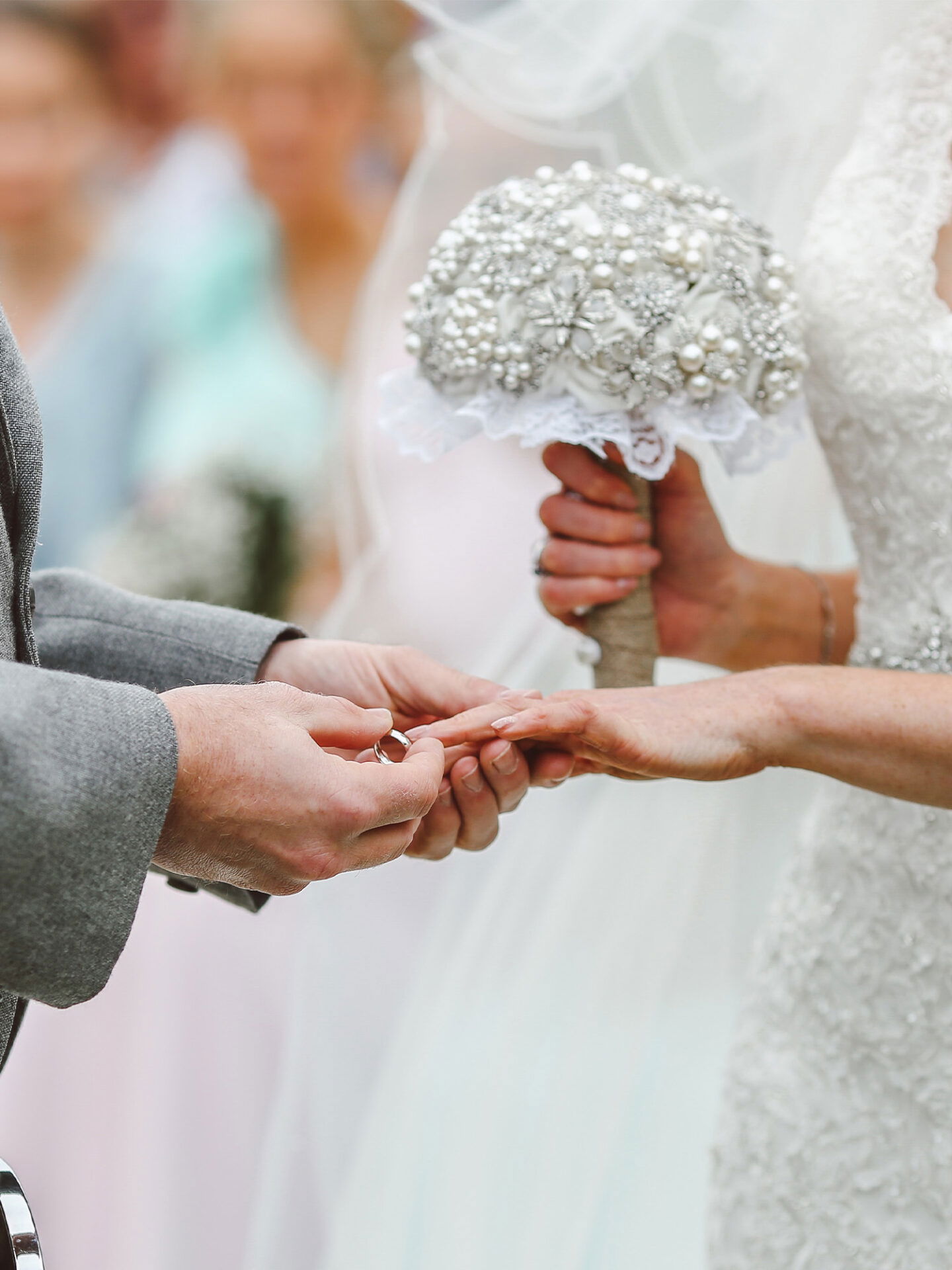 Der emotionale Moment des Ringtauschs, während die Braut einen reich verzierten Strauß aus Perlen und Strass in der Hand hält.