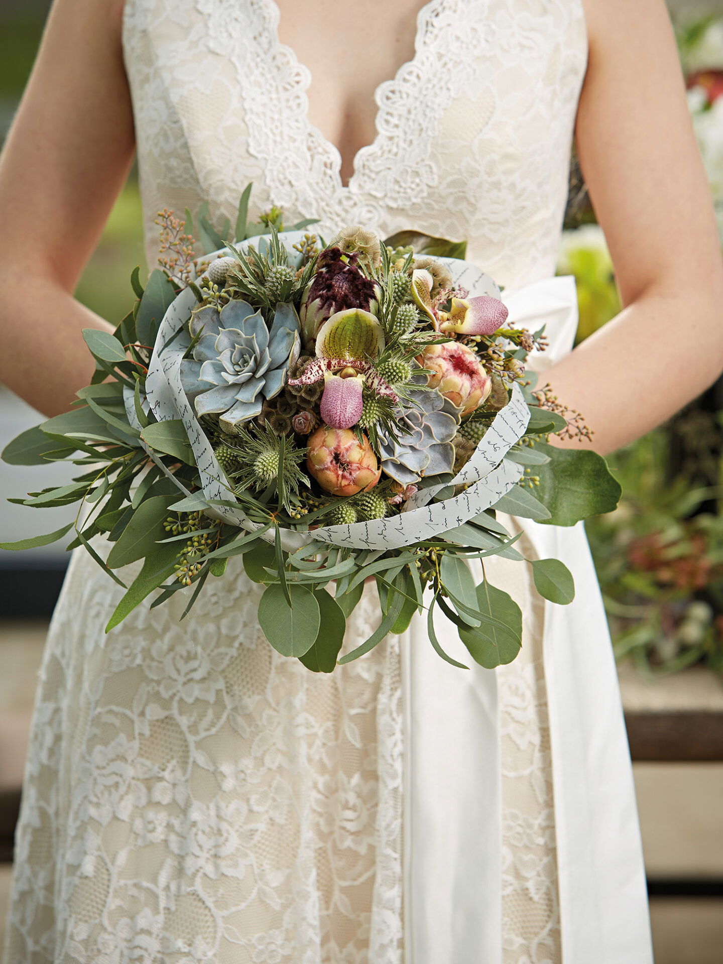 Detailaufnahme eines Hochzeitsstraußes mit Sukkulenten und grünen Akzenten, getragen von einer Braut im eleganten Brautkleid.
