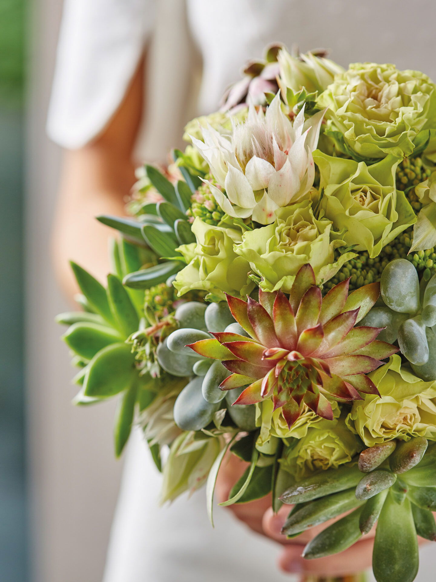 Grüner Brautstrauß mit verschiedenen Sukkulenten und Blumen, passend zum schlichten Brautlook, detailreich fotografiert.