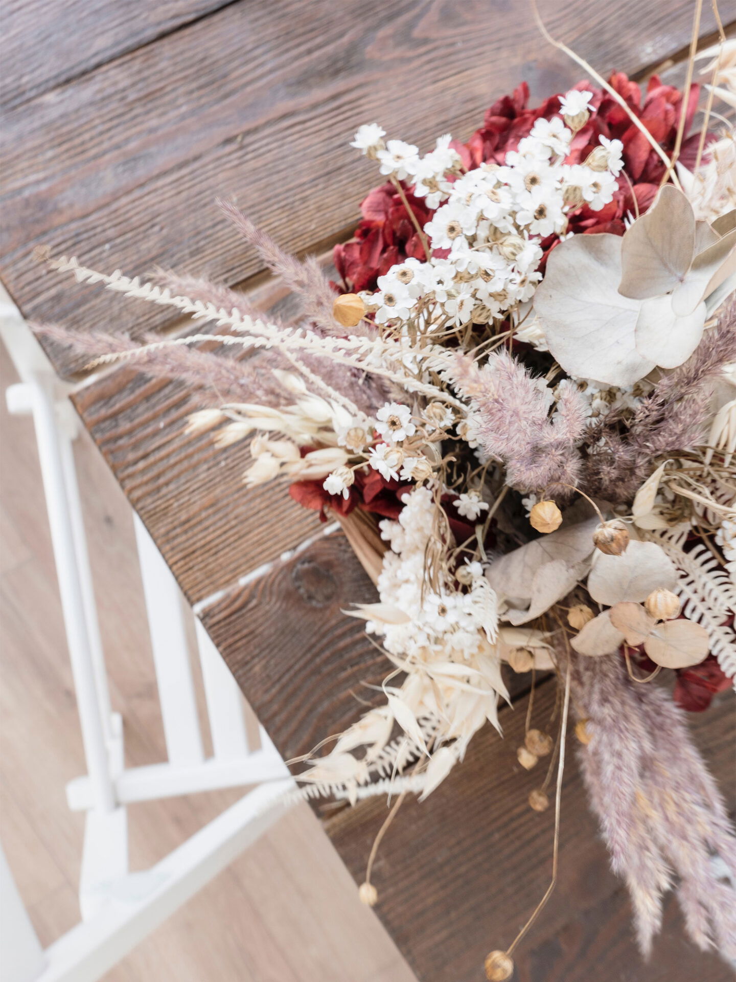 Dekorativer Trockenblumenstrauß mit zarten weißen und roten Blüten, stilvoll auf einem Holztisch arrangiert.