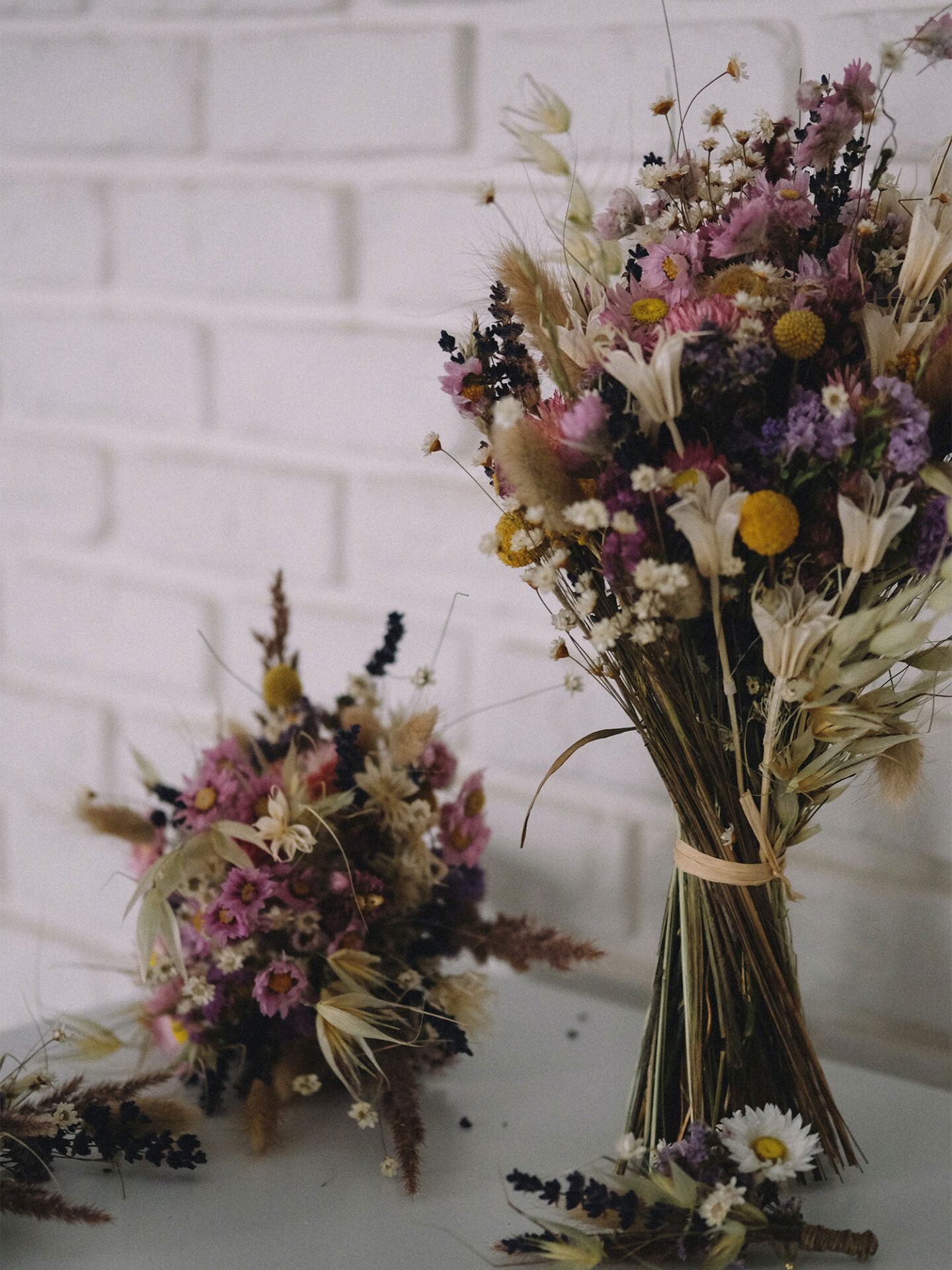 Trockenblumenstrauß mit Wildblumen und Gräsern, arrangiert vor einer weißen Mauer, ideal als Hochzeitsdekoration.