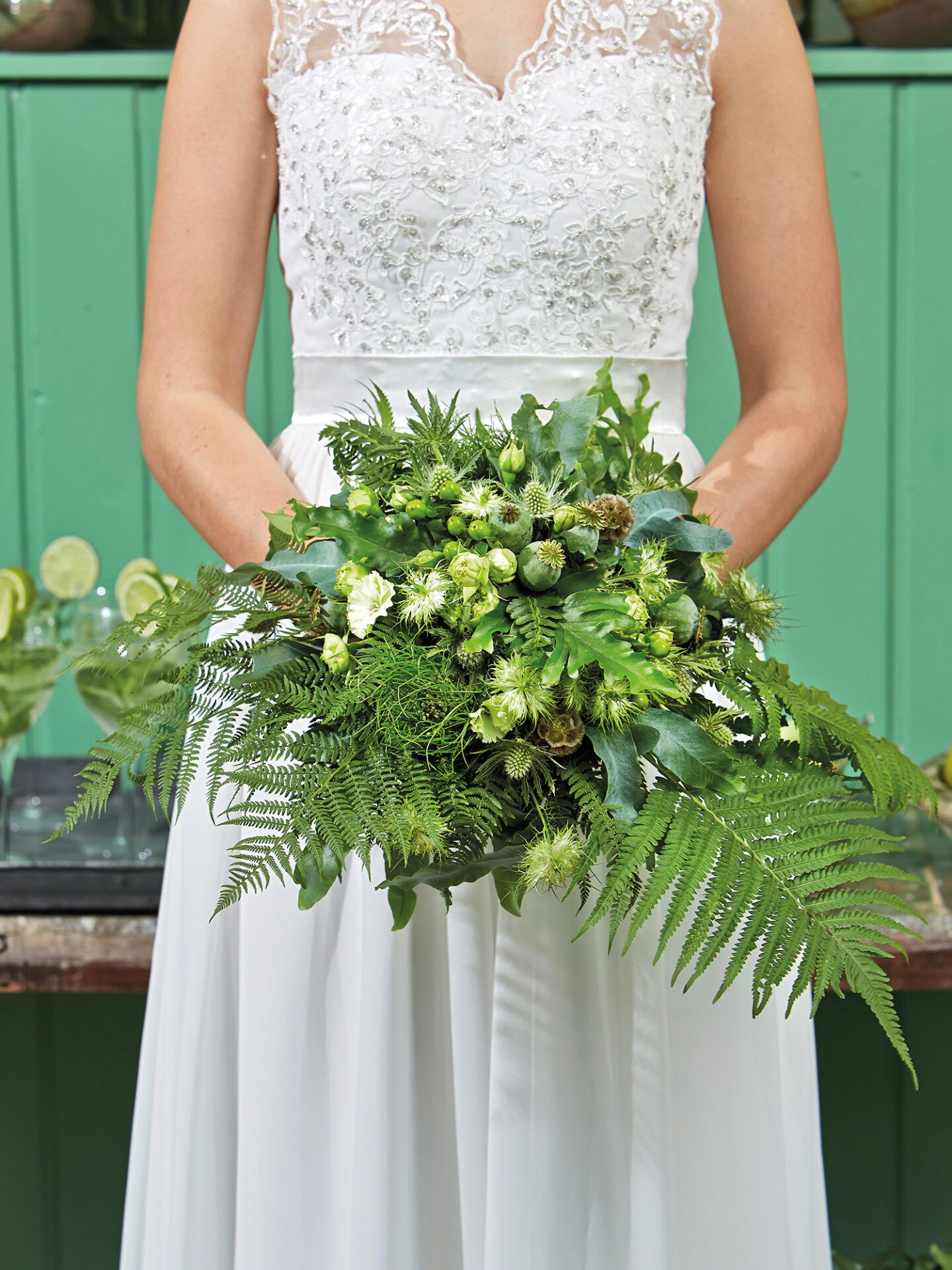 Nahaufnahme eines grünen Brautstraußes mit verschiedenen Farnen, stacheligen Disteln und Knospen, die die natürliche Schönheit des Straußes betonen.