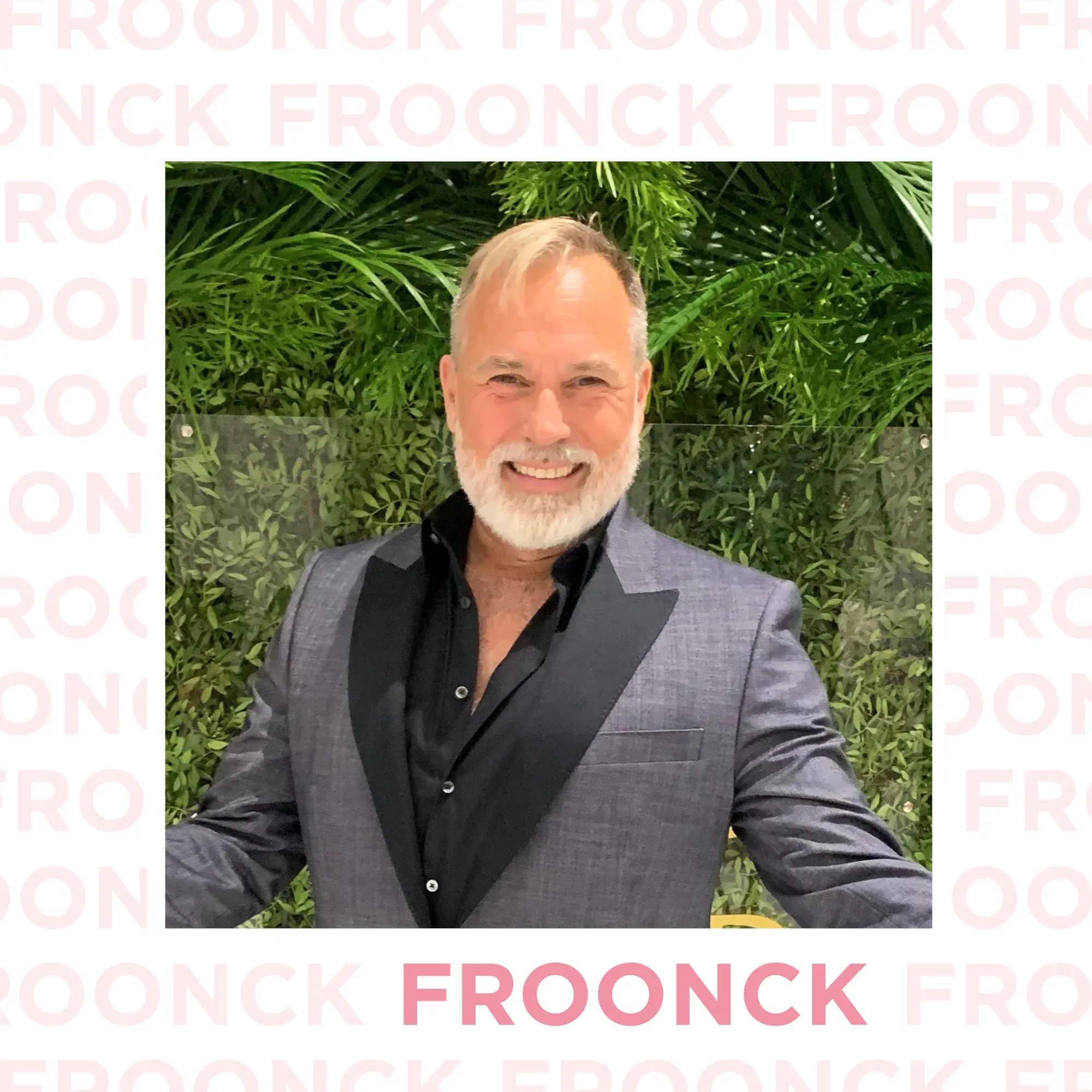 Der Hochzeitsprofi Froonck posiert lächelnd in einem schicken grauen Anzug mit schwarzem Hemd vor einer üppigen Pflanzenwand. Sein stilvolles Auftreten unterstreicht seine Expertise im Hochzeitsbereich.